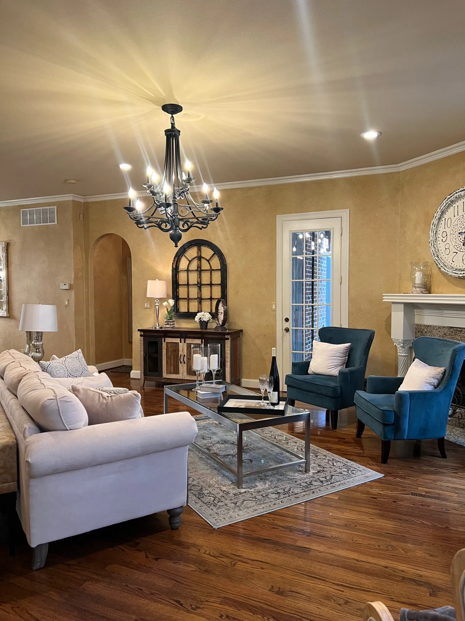 Spacious living area featuring wood-finish flooring, a decorative fireplace with a stone surround, and an elegant chandelier