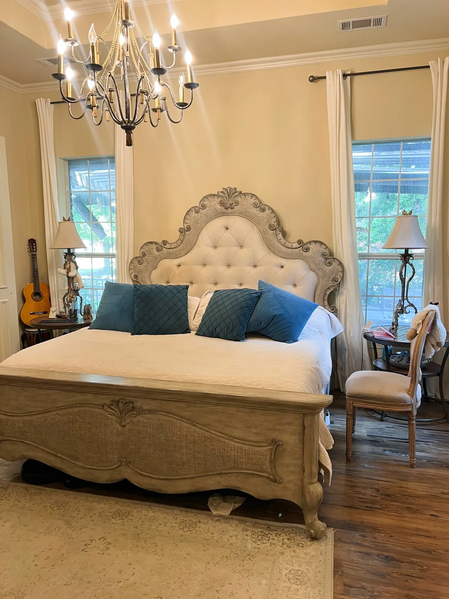 Recessed ceiling with an ornate chandelier, two large windows with drapes, and wood-finish flooring