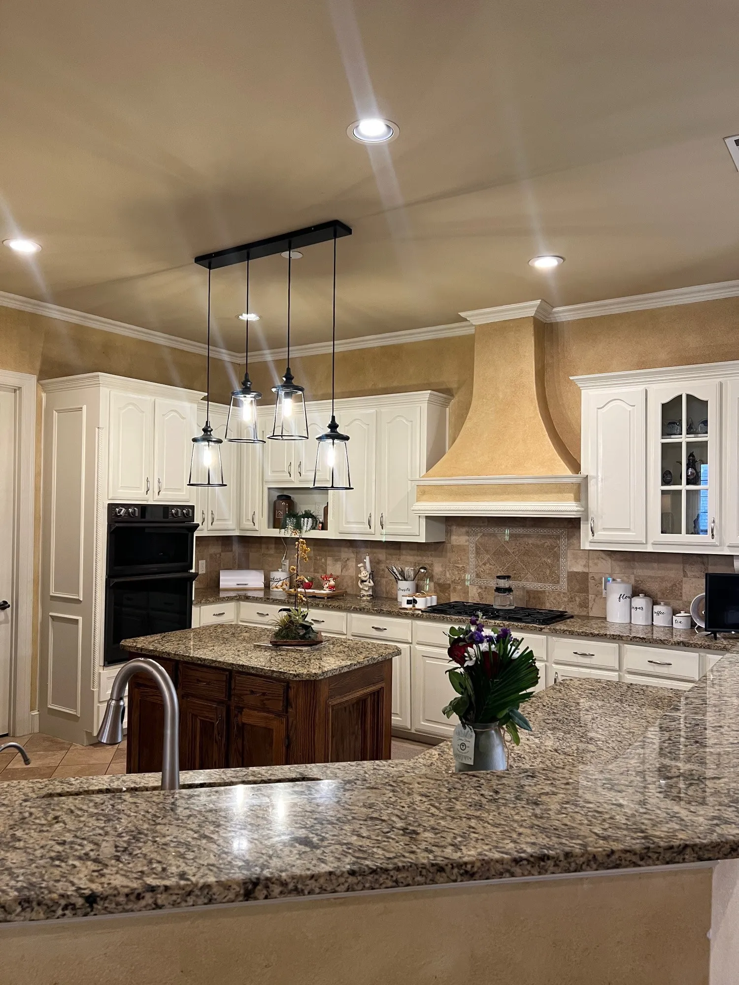 Well-appointed kitchen featuring granite countertops, white cabinetry, a built-in double oven, and a central island with an undermount sink