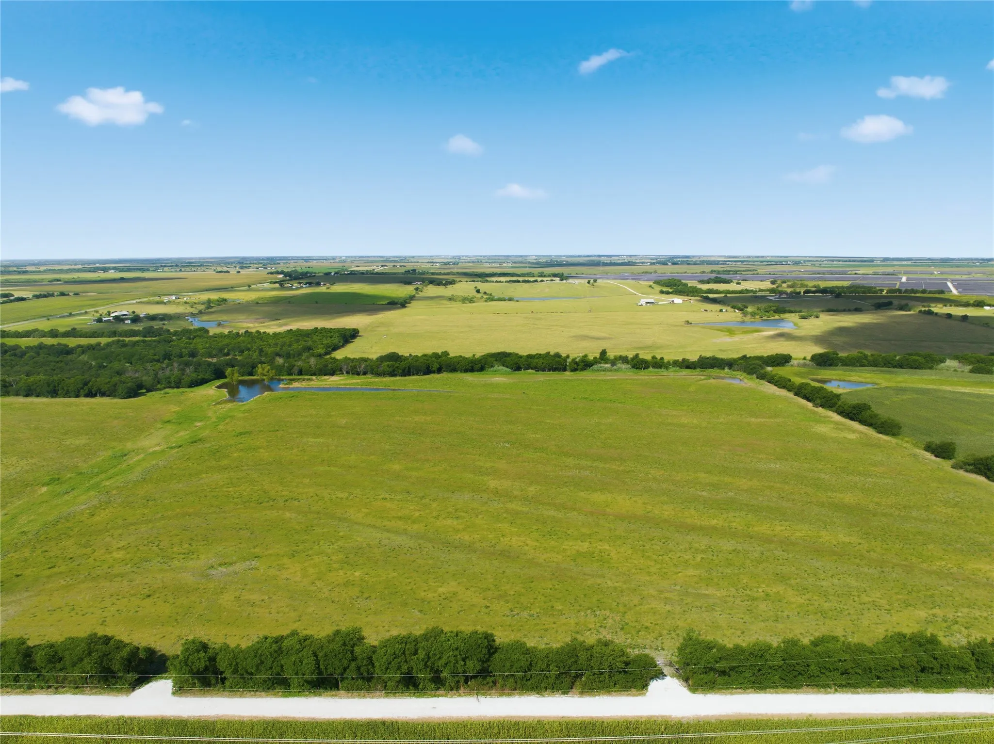 Expansive agricultural land featuring a verdant landscape, mature treelines, and multiple water features