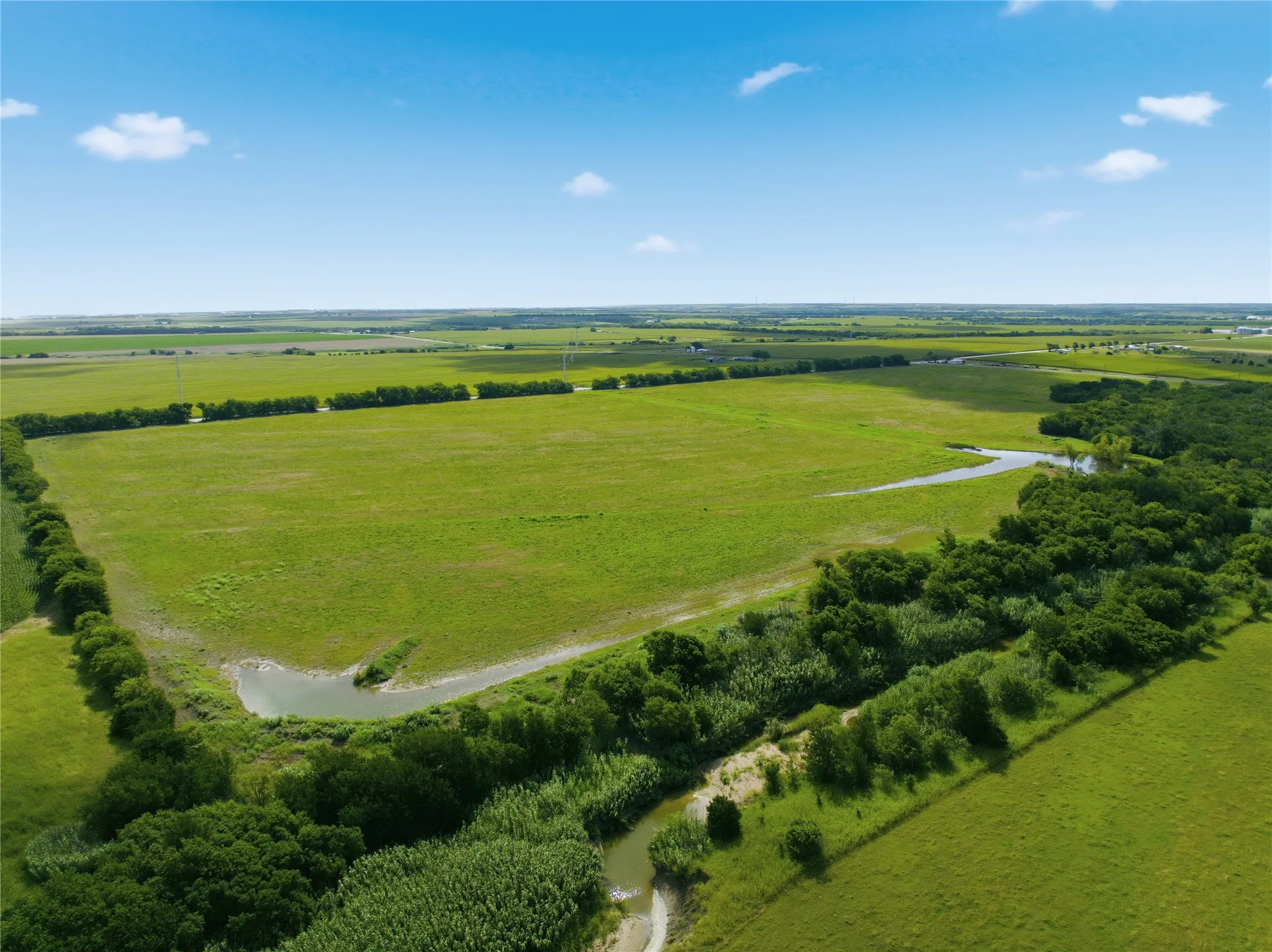Expansive green fields featuring natural waterways and a tree-lined border