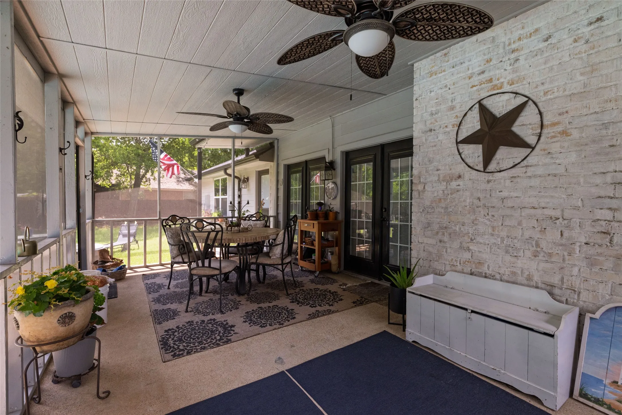 Screened porch featuring a painted brick accent wall and two ceiling fans