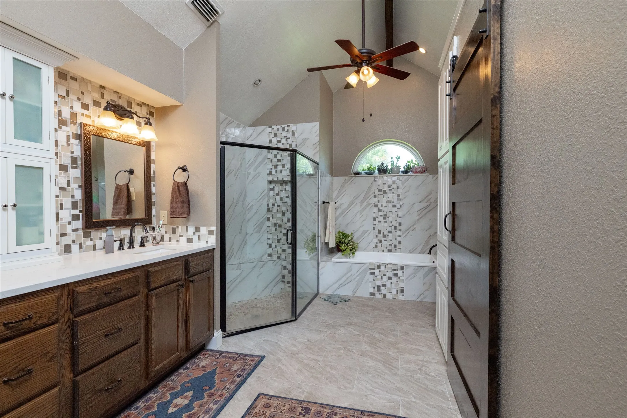 Spacious bathroom featuring a vaulted ceiling, wood-finish ceiling fan, and a barn door entry