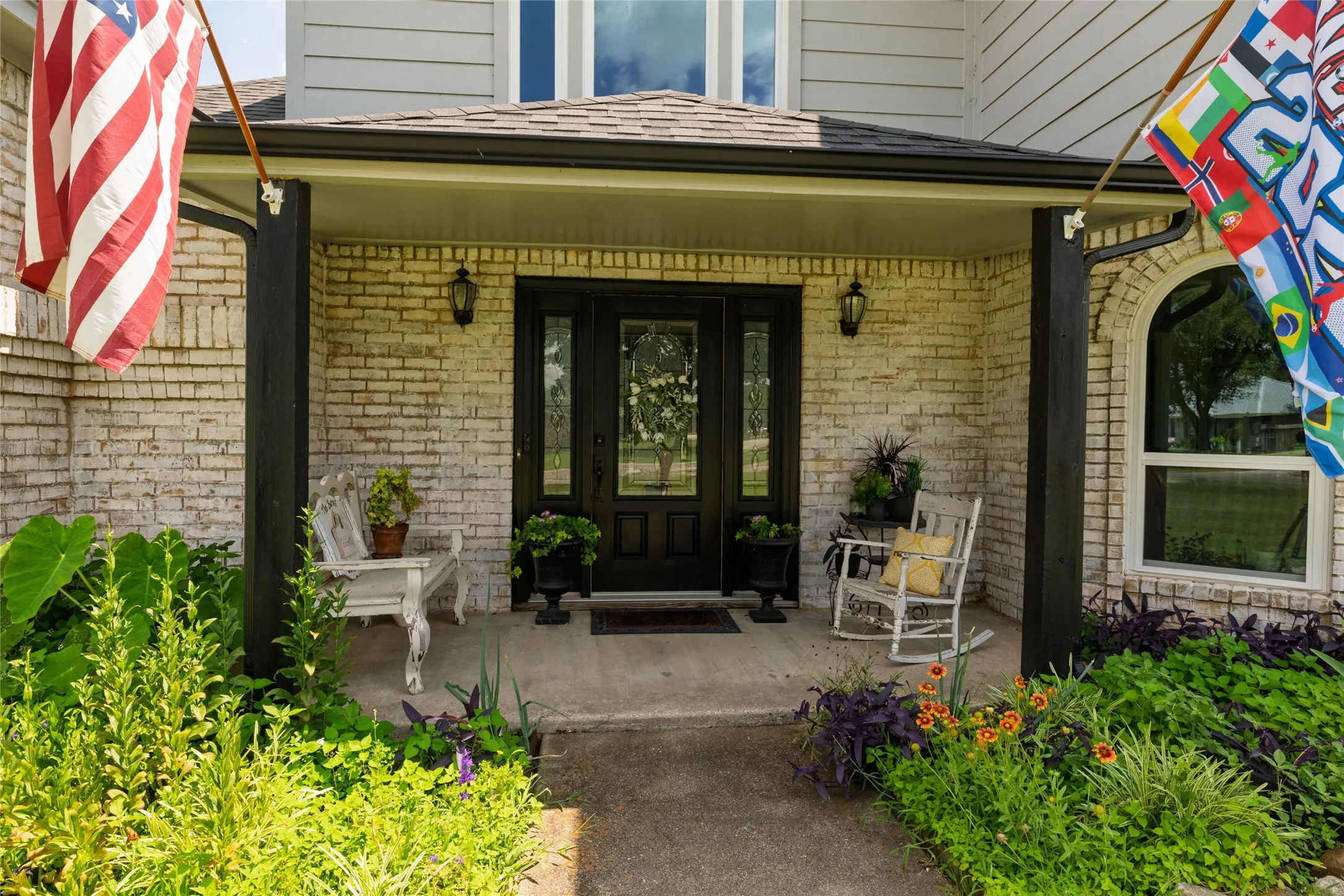 Front porch featuring white-washed brick, black columns, and a dark paneled entry door with sidelights