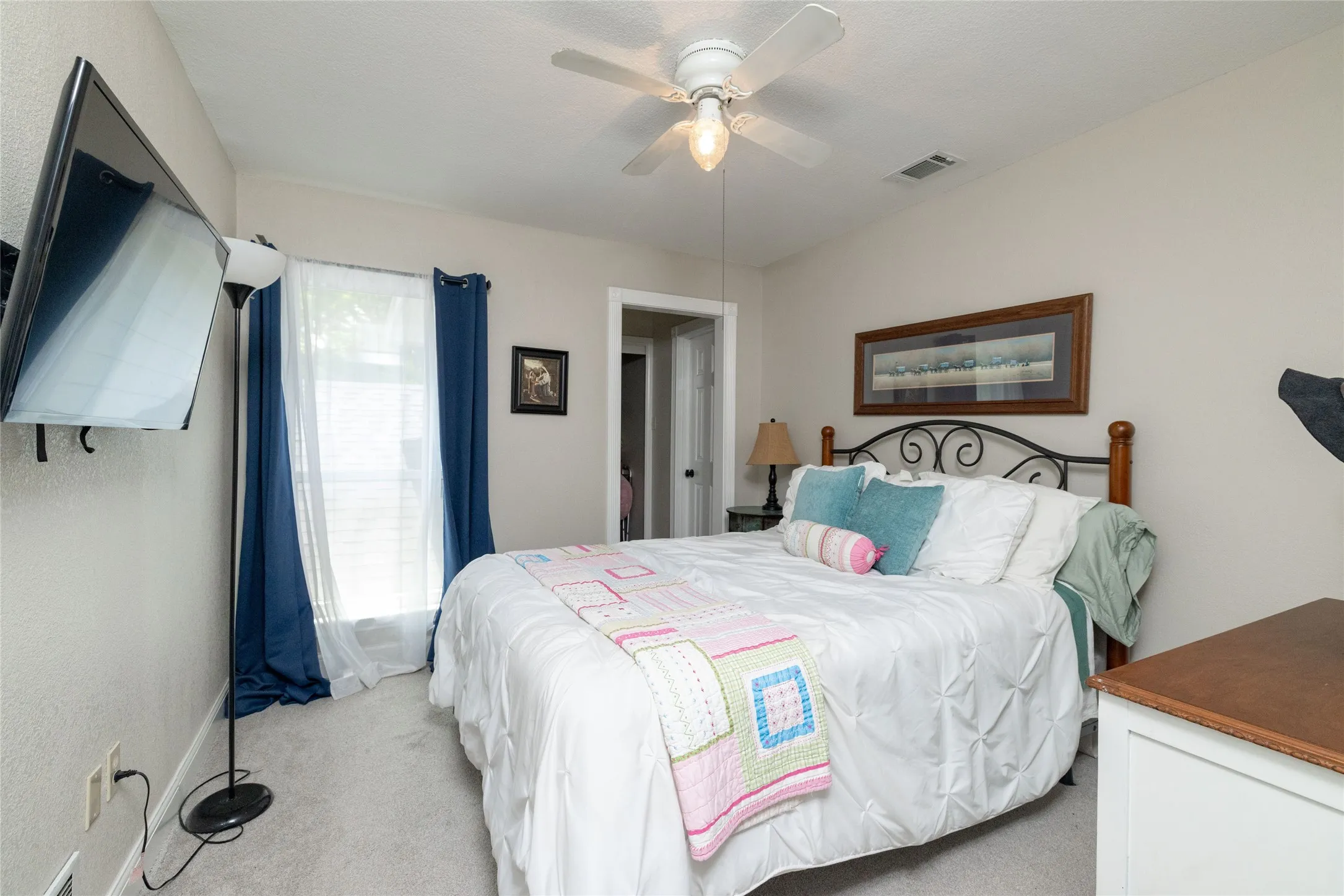 Carpeted interior space featuring a ceiling fan with integrated lighting, wall-mounted television bracket, window with blinds, and painted walls