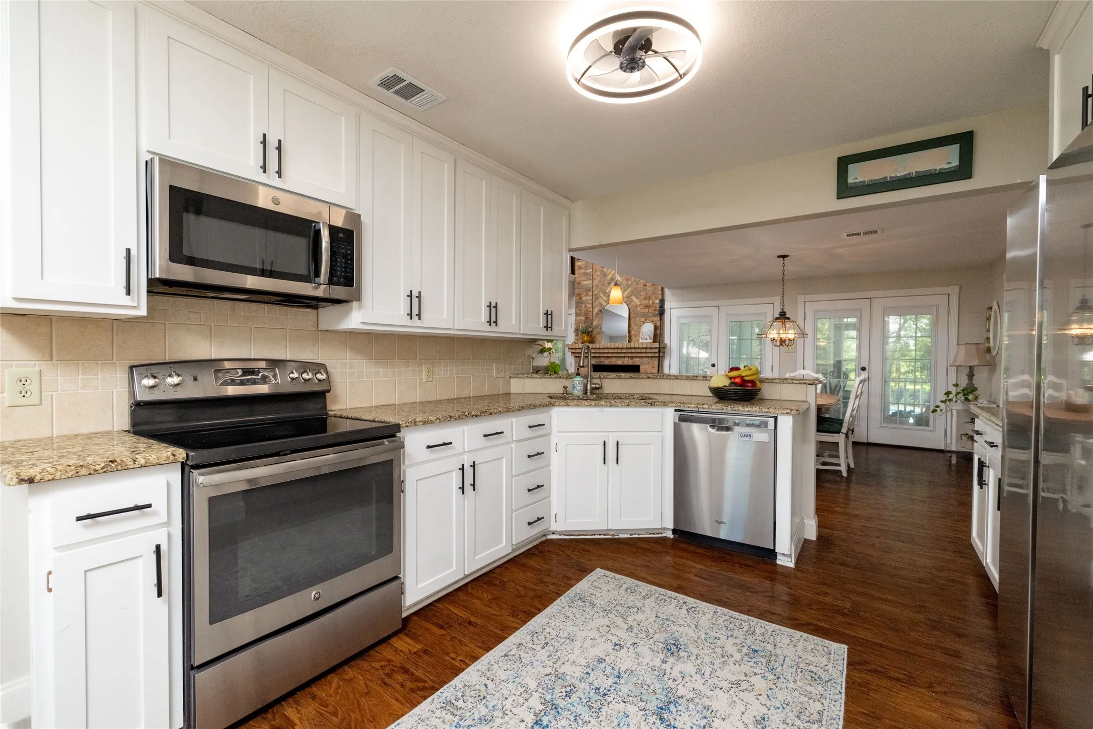 Modern kitchen featuring white shaker-style cabinetry, granite countertops, stainless steel appliances, wood-finish flooring, and a tile backsplash