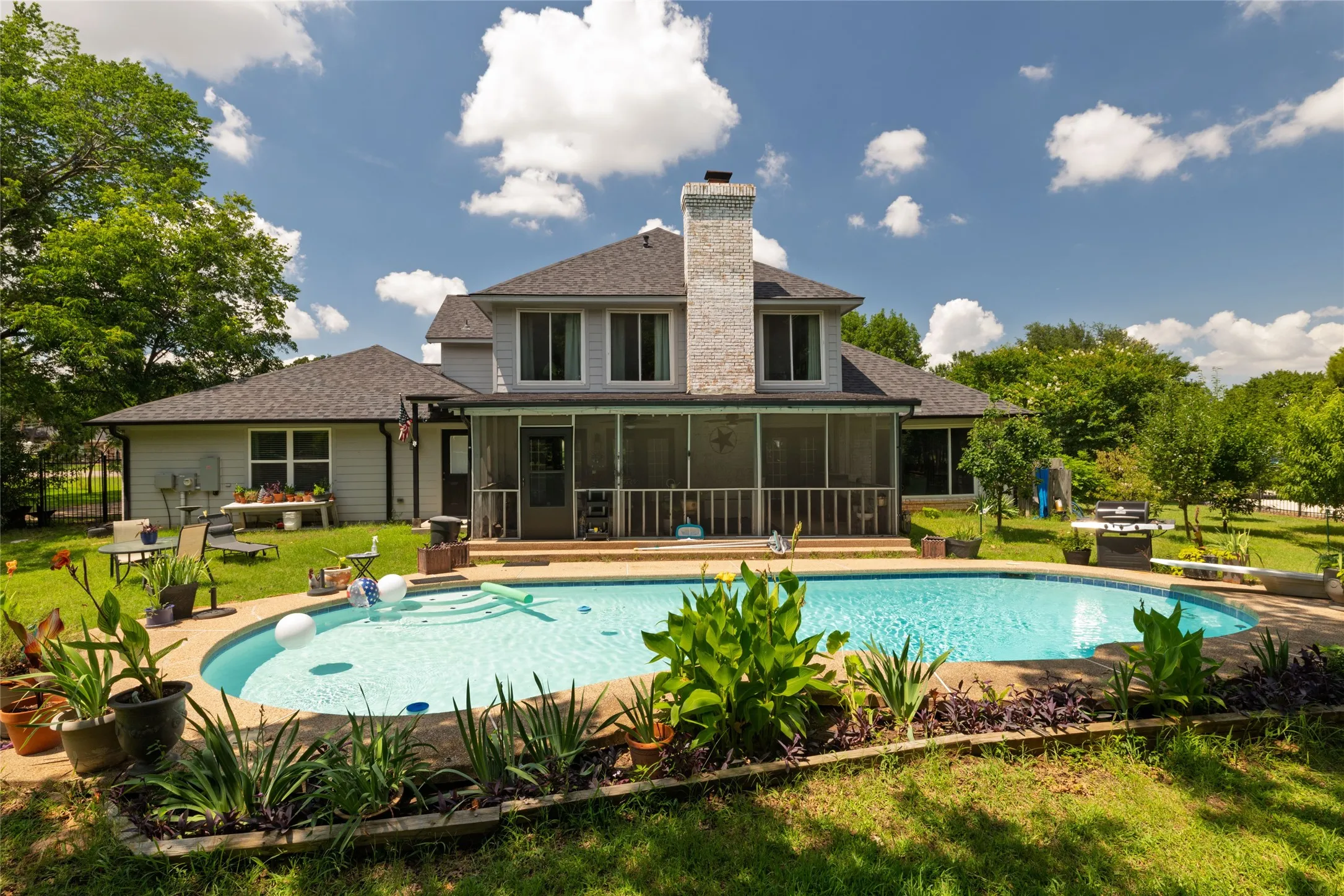Spacious backyard featuring an in-ground swimming pool with stone coping, a screened porch, and mature landscaping