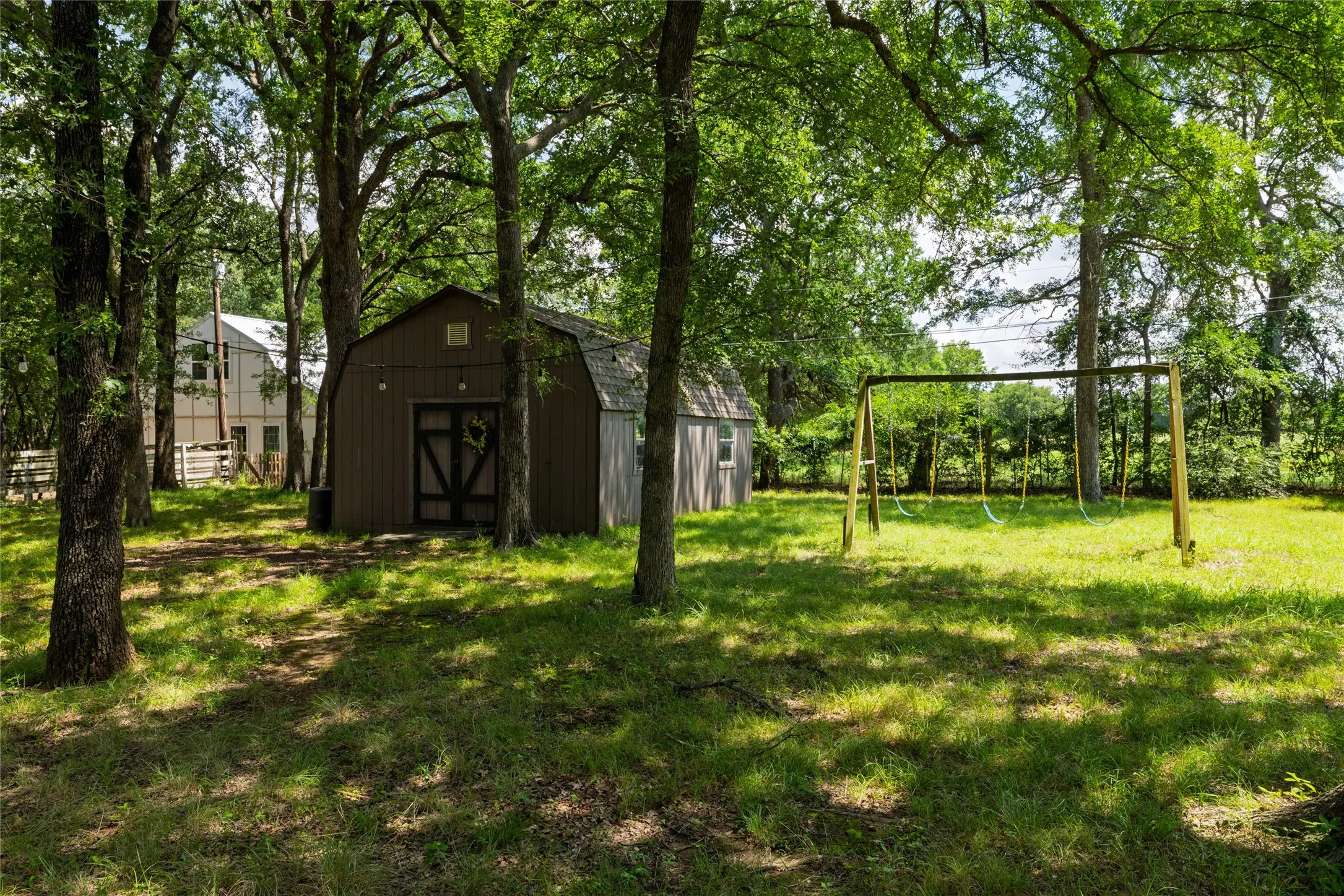 Expansive outdoor space featuring a detached storage shed, lush green lawn, and mature trees providing natural shade