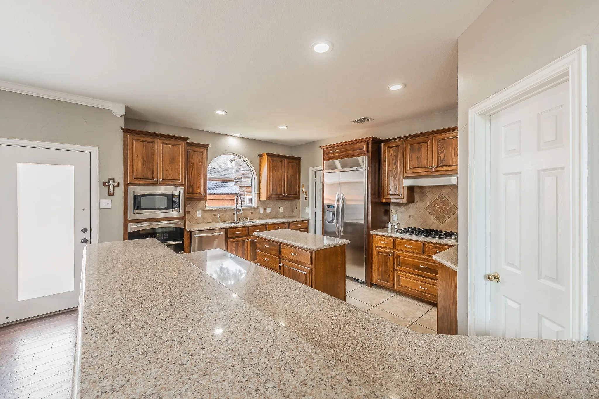 Kitchen featuring a large breakfast bar, wood cabinetry, built-in stainless steel appliances, a center island, and an arched window above the sink