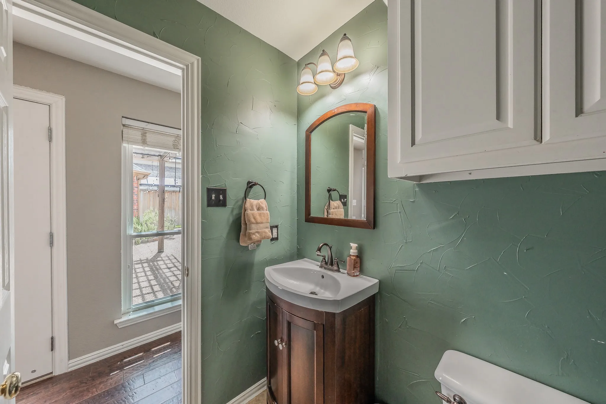 Powder room featuring a corner vanity with a built-in sink, dark wood-finish cabinetry, and a framed arch-top mirror