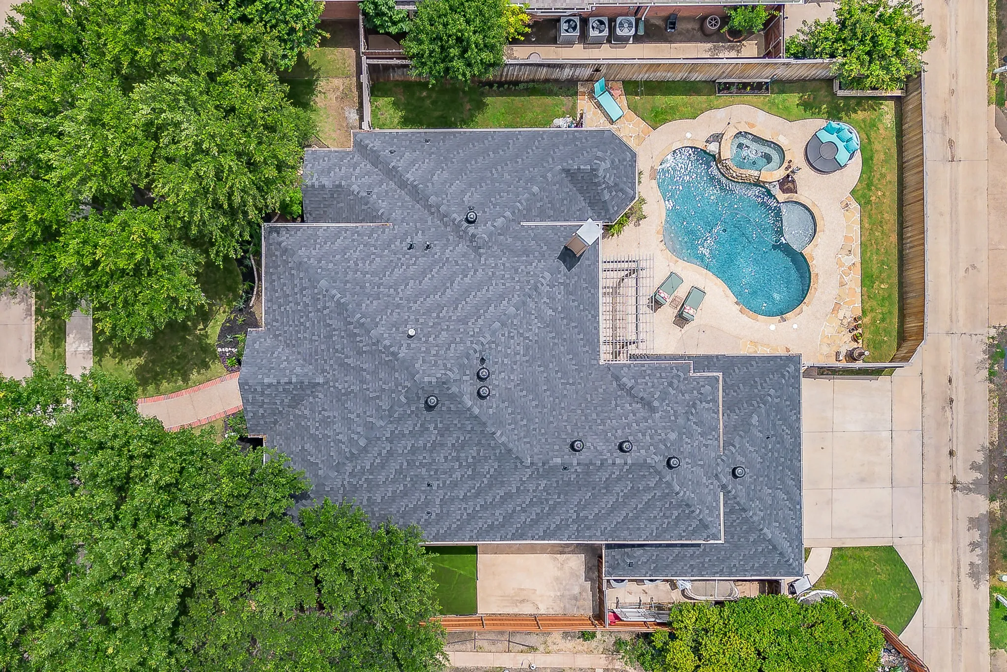 Rear exterior featuring a freeform swimming pool with integrated spa and surrounding stone-look decking