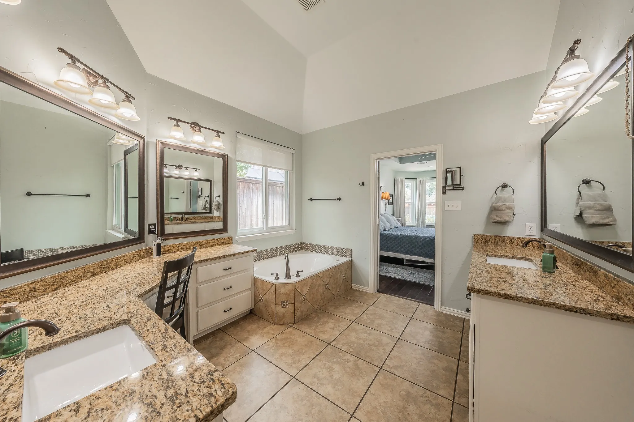 Bathroom featuring a vaulted ceiling, dual vanity sinks with stone countertops, a built-in makeup vanity, a corner soaking tub, and tile flooring