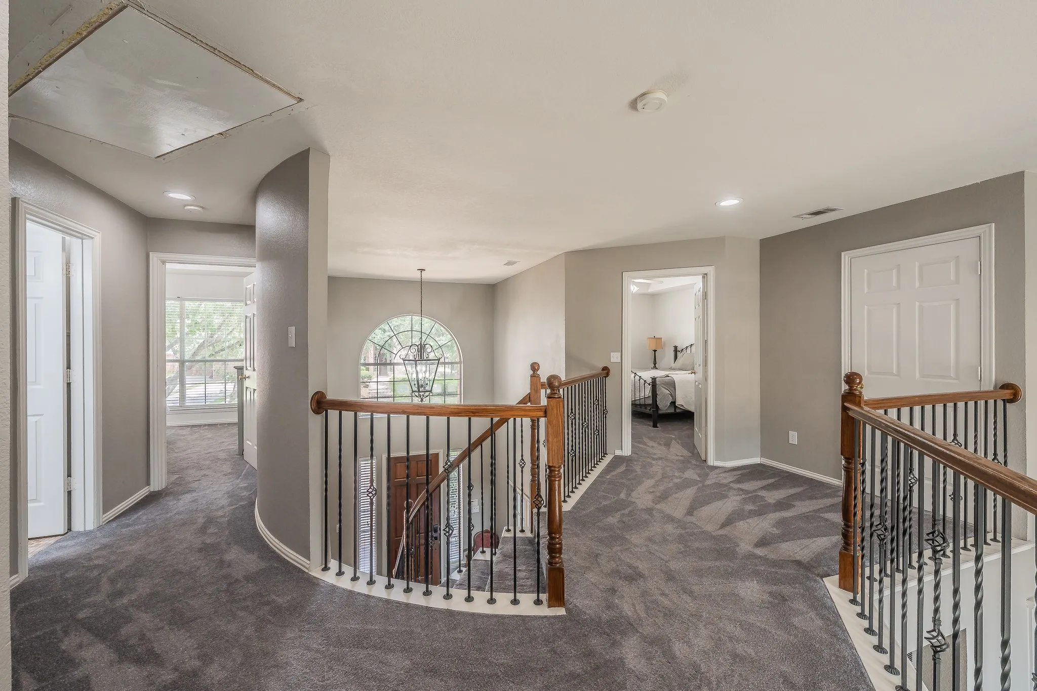 Spacious upper-level landing featuring gray patterned carpeting, recessed lighting, and a prominent arched window with a chandelier
