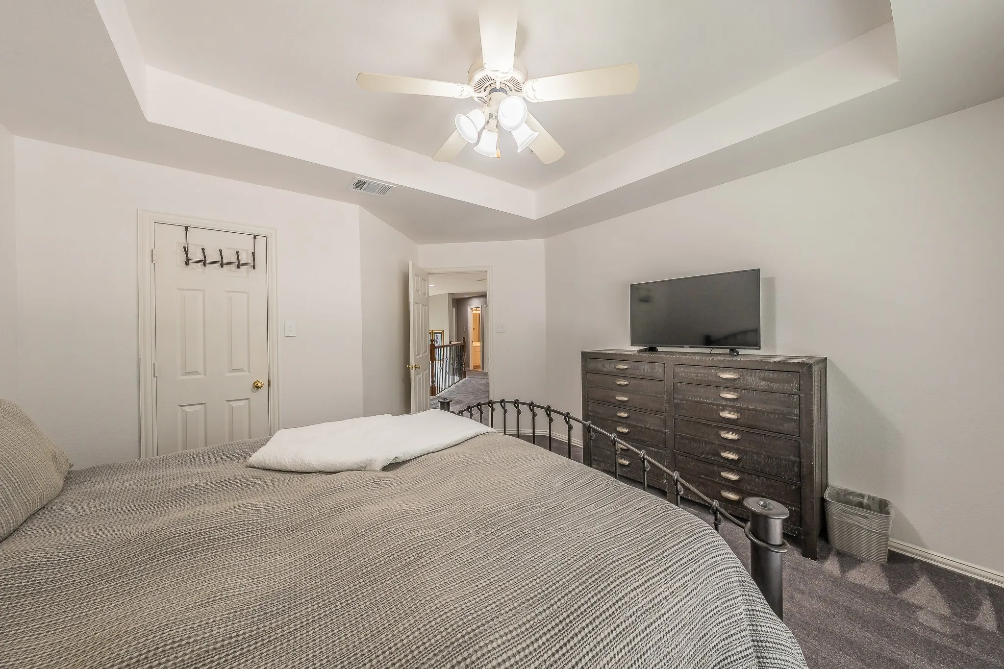 Room featuring a tray ceiling with a ceiling fan, white walls, and gray patterned carpet