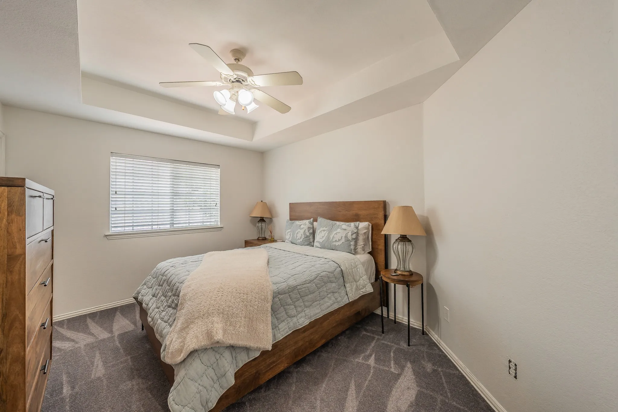 Room featuring a tray ceiling with a ceiling fan, a window with horizontal blinds, and patterned carpeting