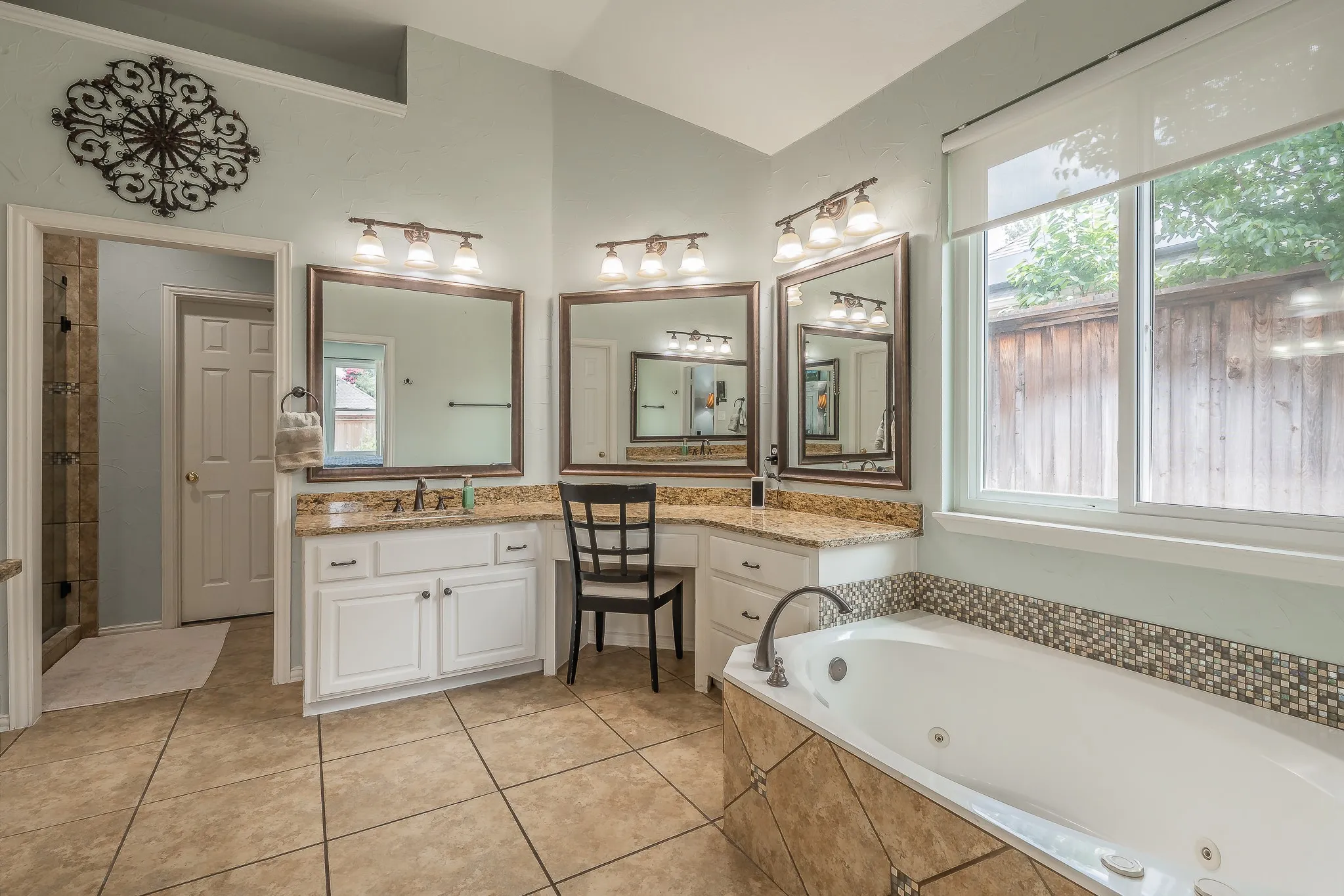 Spacious bathroom featuring a built-in jetted tub with mosaic tile surround, dual vanity with stone-finish countertops, tiled flooring, and a separate shower enclosure