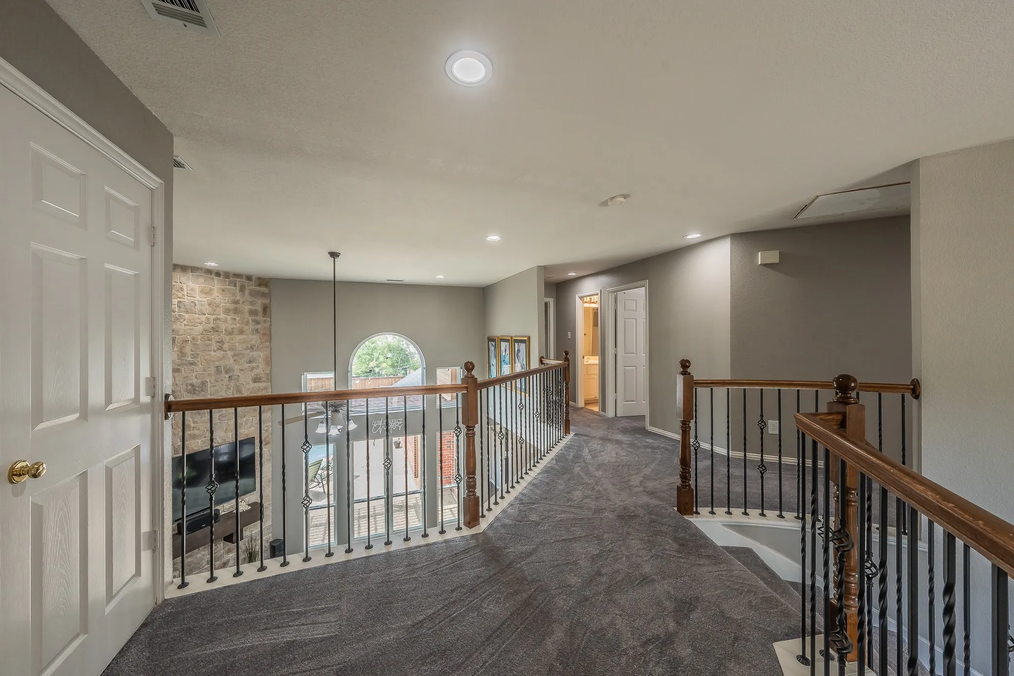 Upper-level landing featuring textured gray carpeting, recessed lighting, and a wrought iron and wood balustrade overlooking a lower-level living space
