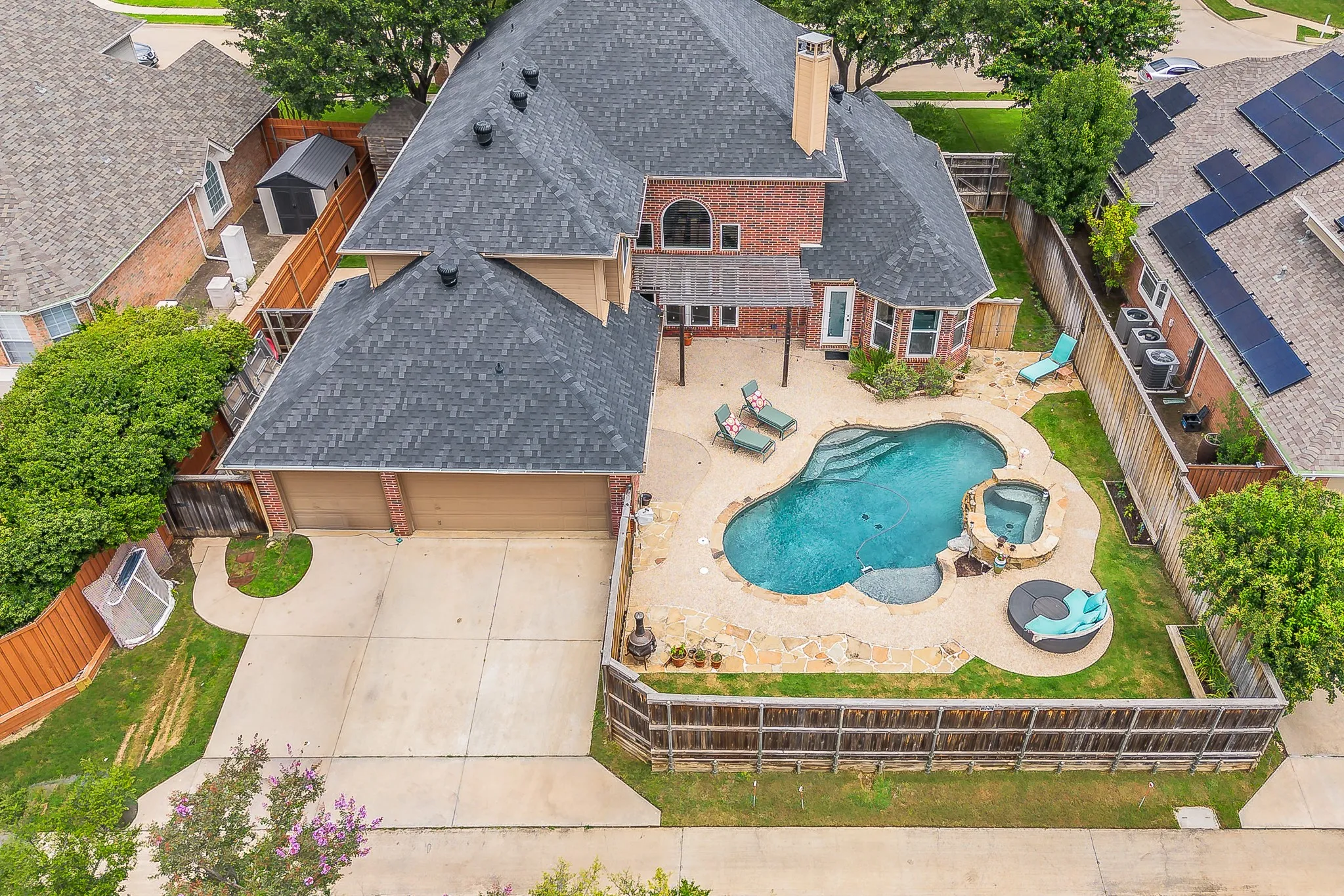Aerial perspective showcasing a brick residence with a dark shingle roof, a concrete driveway, and a two-car garage