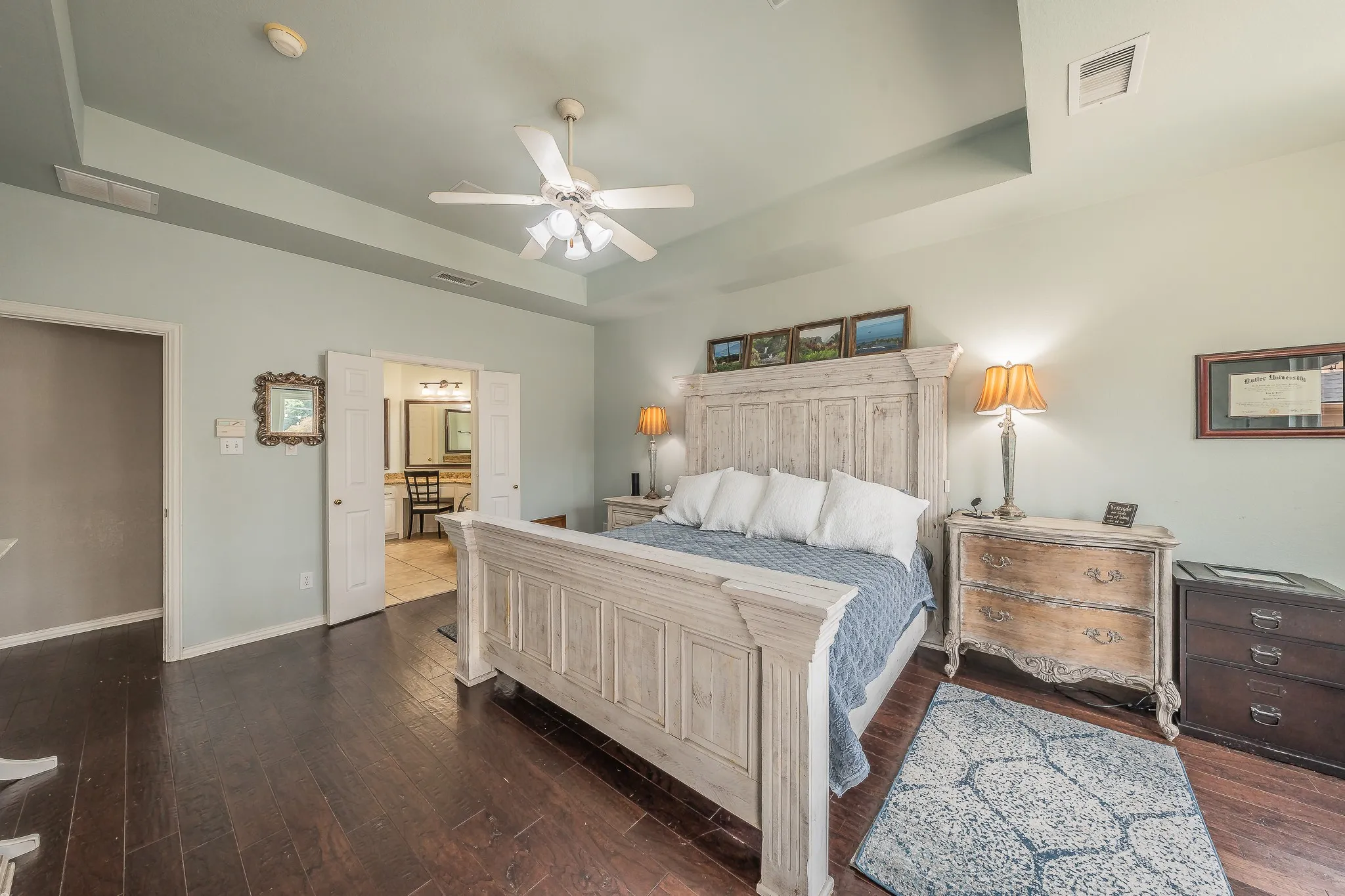 Spacious bedroom featuring dark wood-finish flooring, a tray ceiling, and a ceiling fan