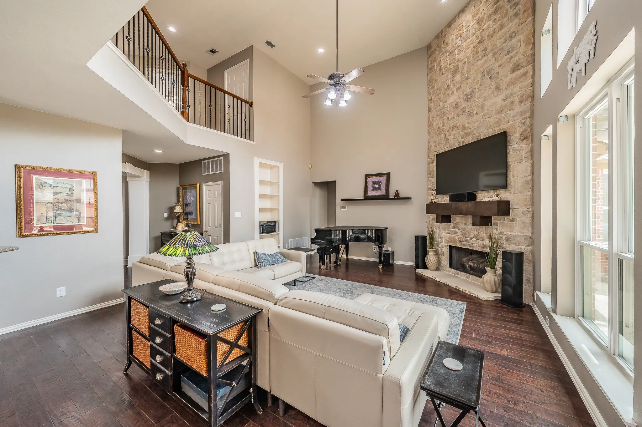 Vaulted living area featuring a stone fireplace with a wood mantle, an upstairs balcony overlooking the space, wood-finish flooring, and large windows
