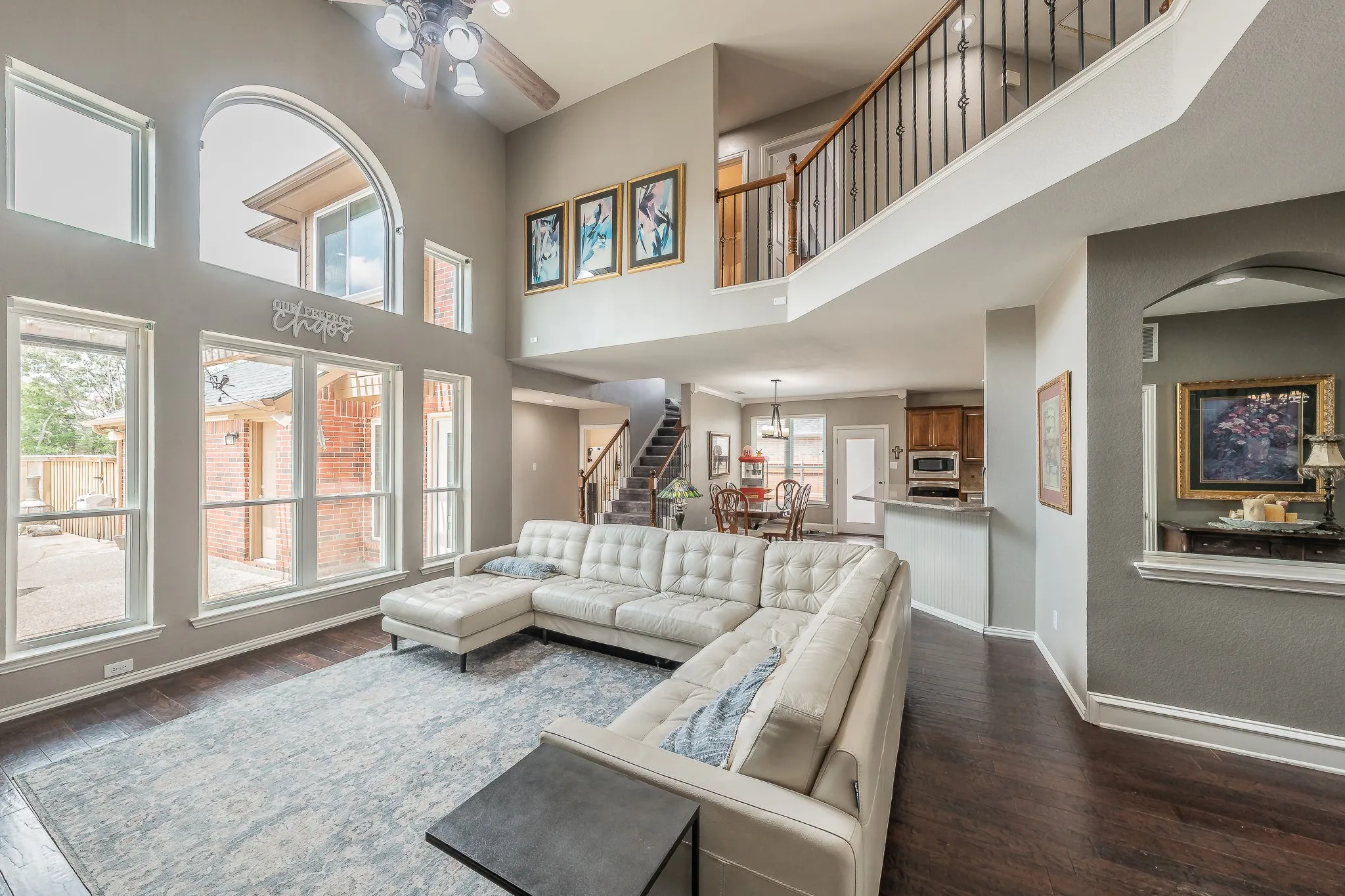 Two-story living area featuring dark wood-finish flooring, a vaulted ceiling with a fan light fixture, and an arched window