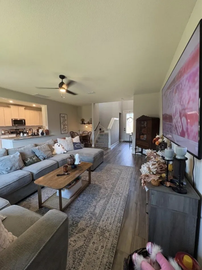 Open concept living area featuring wood-finish flooring, a ceiling fan with integrated lighting, and a kitchen pass-through with light-toned cabinetry