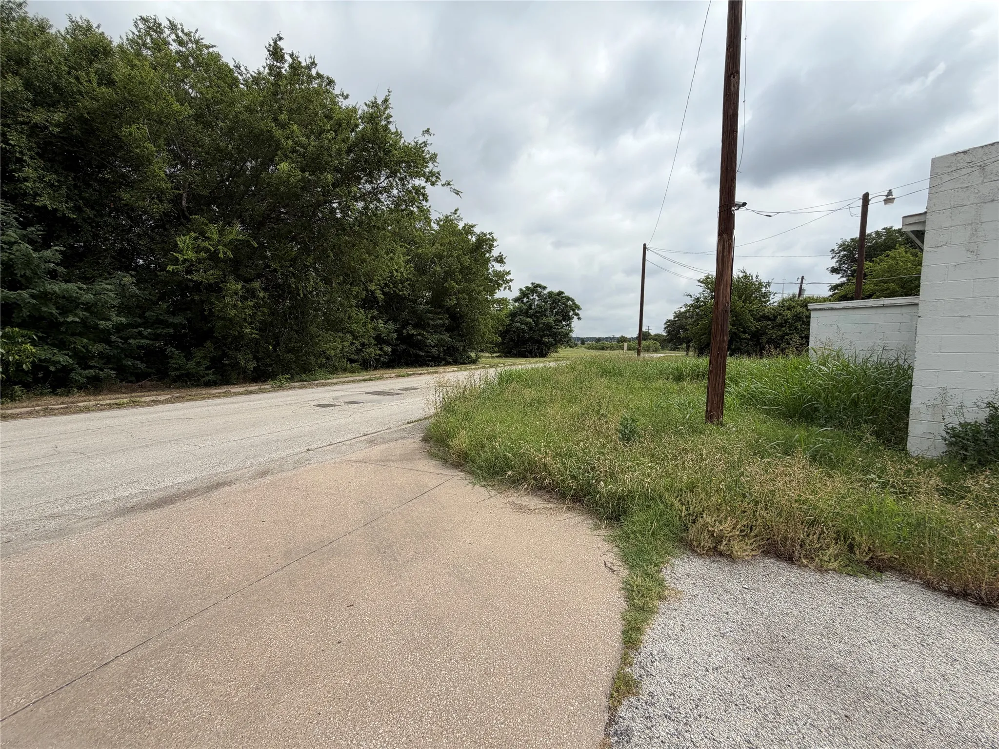 Asphalt road with an unpaved shoulder, green foliage, and utility poles