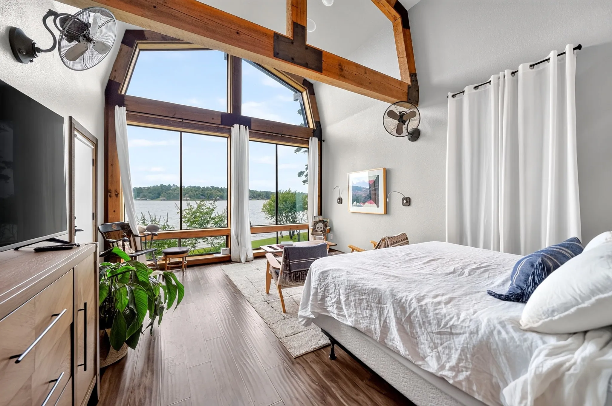 Vaulted ceilings with exposed wood beams, extensive floor-to-ceiling windows, wood-finish flooring, and white privacy curtains