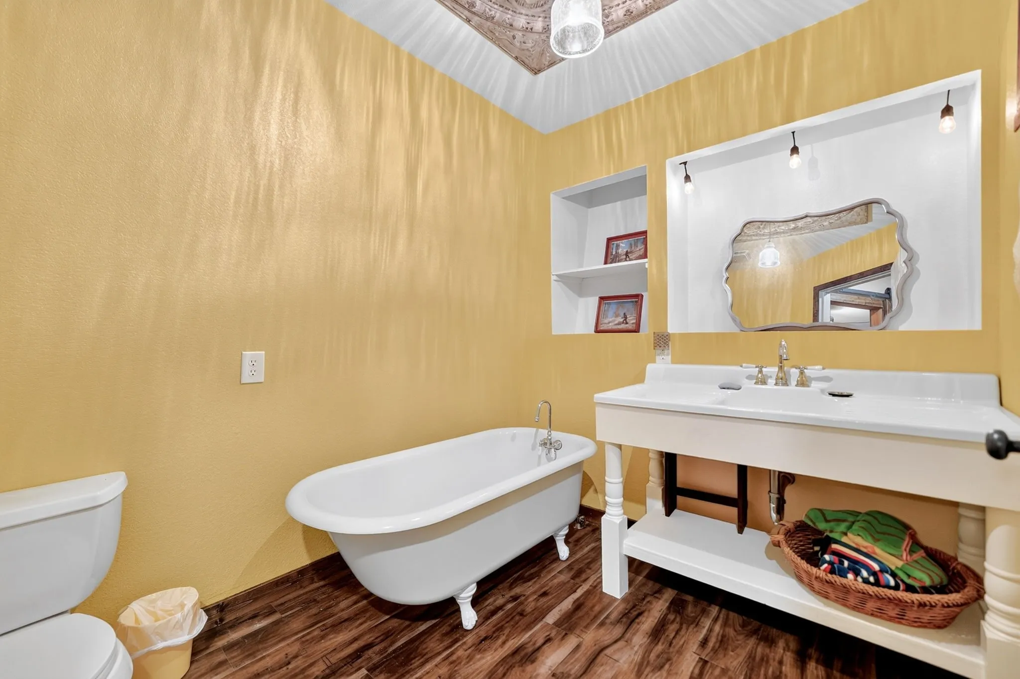 Bathroom featuring a clawfoot tub, wood-finish flooring, a wall-mounted vanity with integrated sink, and recessed wall shelving