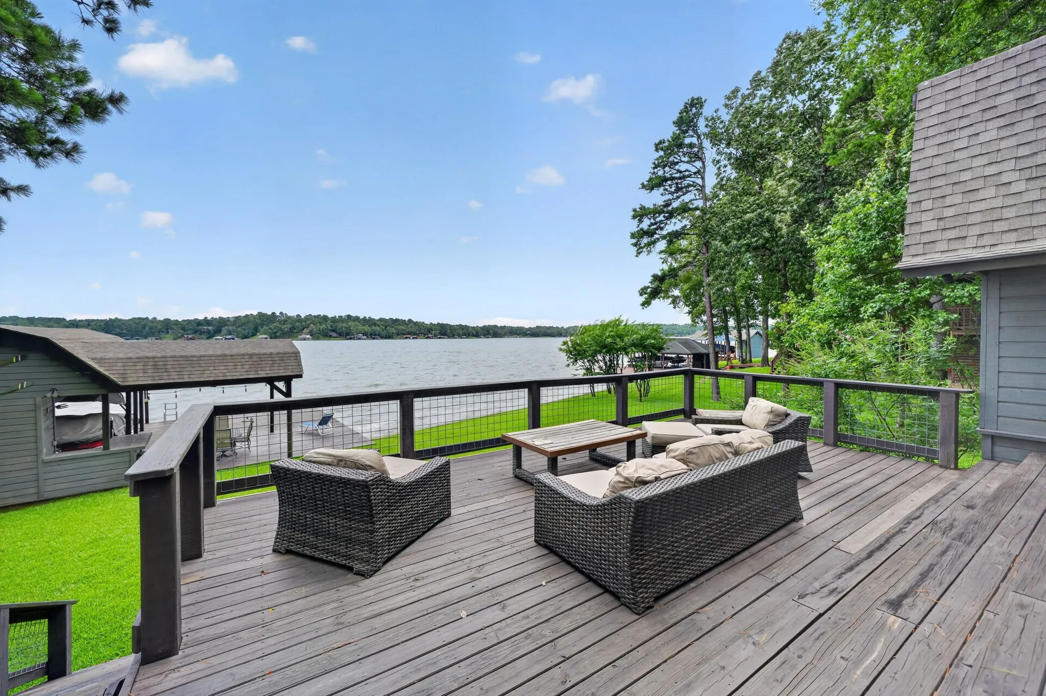 Expansive wooden deck overlooking a lake, featuring a railing with wire infill