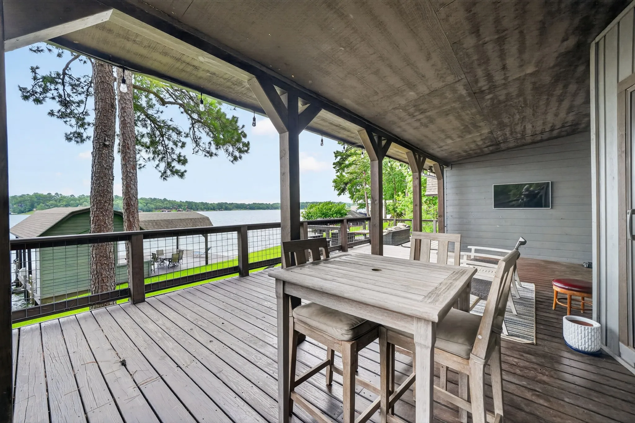 Expansive covered deck featuring wood-finish flooring, dark wood columns, and a railing with metal grid infill