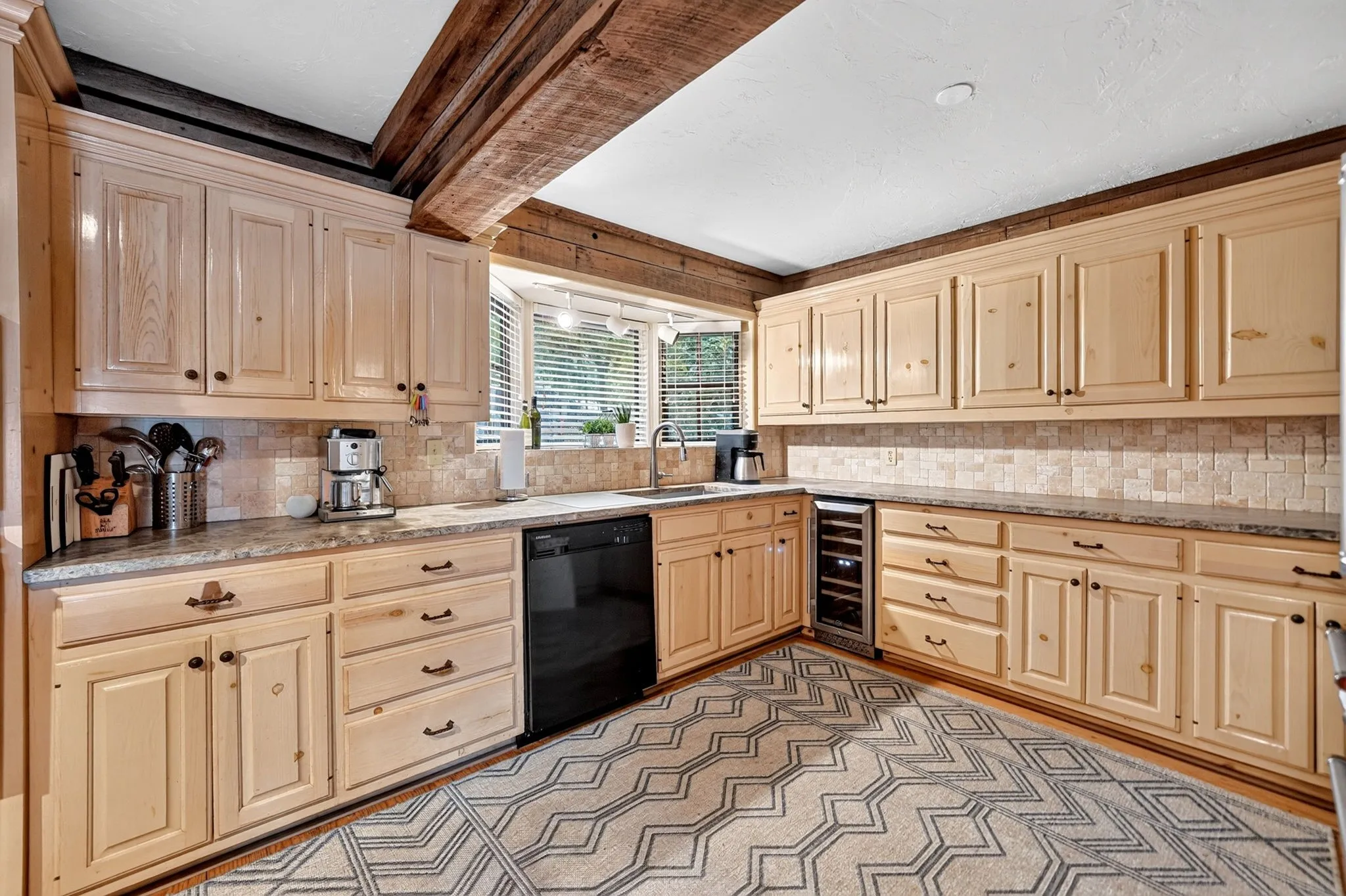 Kitchen featuring light wood cabinetry, stone-finish countertops, a tile backsplash, and exposed wood ceiling beams