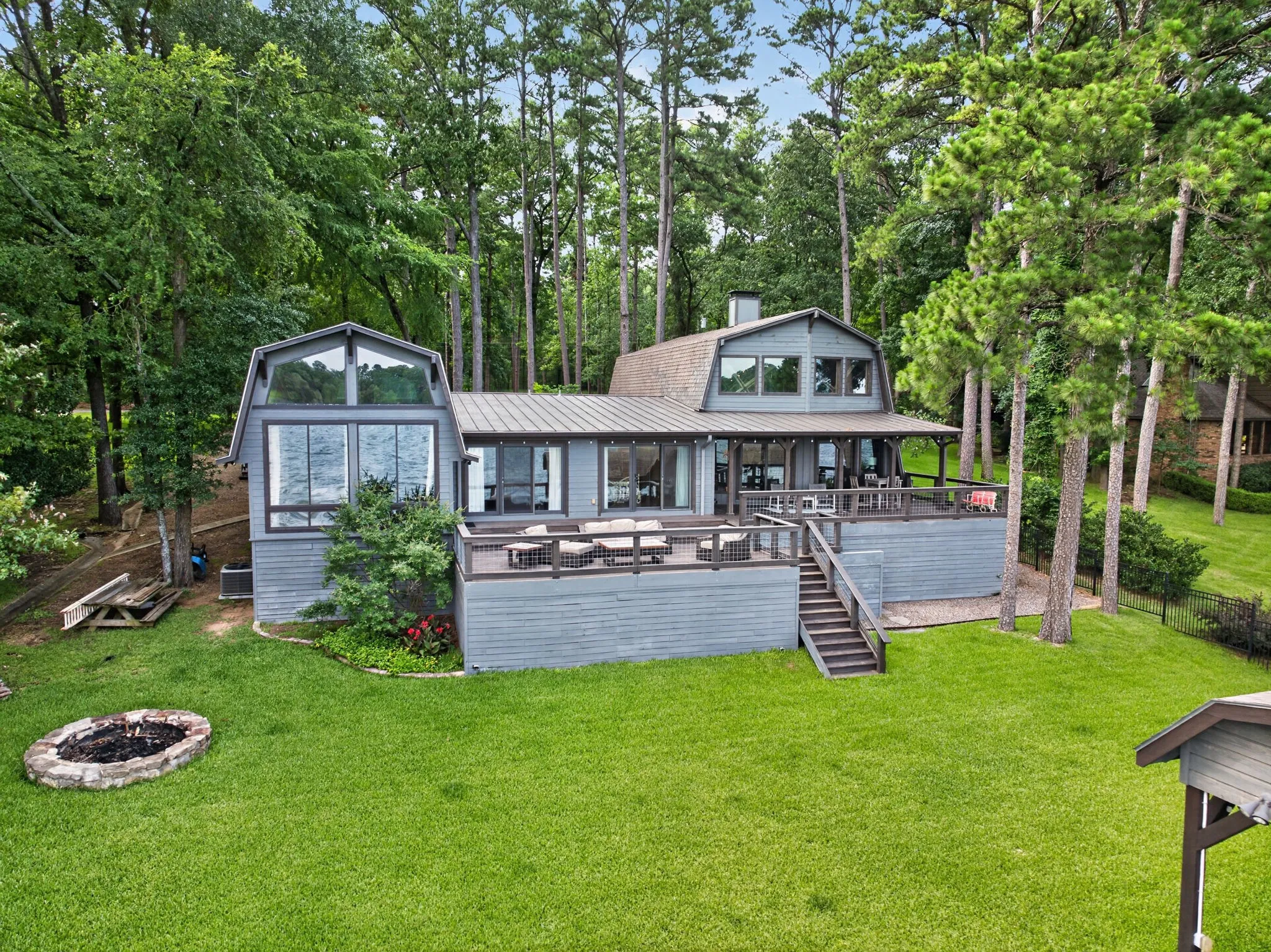 Waterfront residence featuring extensive decking, a stone fire pit, and a spacious green lawn