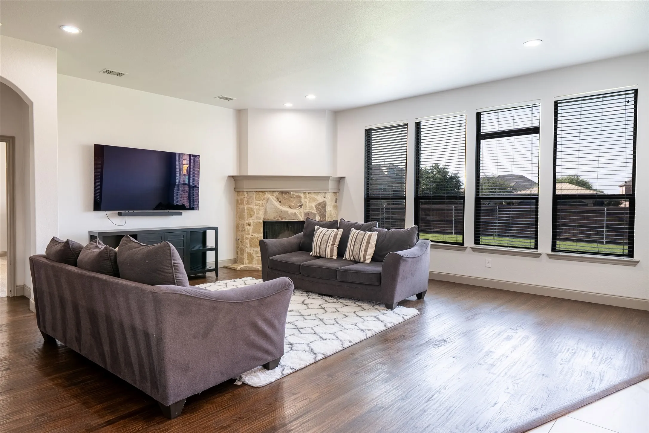 Living area featuring rich wood-finish flooring, a stone fireplace with a substantial hearth, and a wall of three large windows