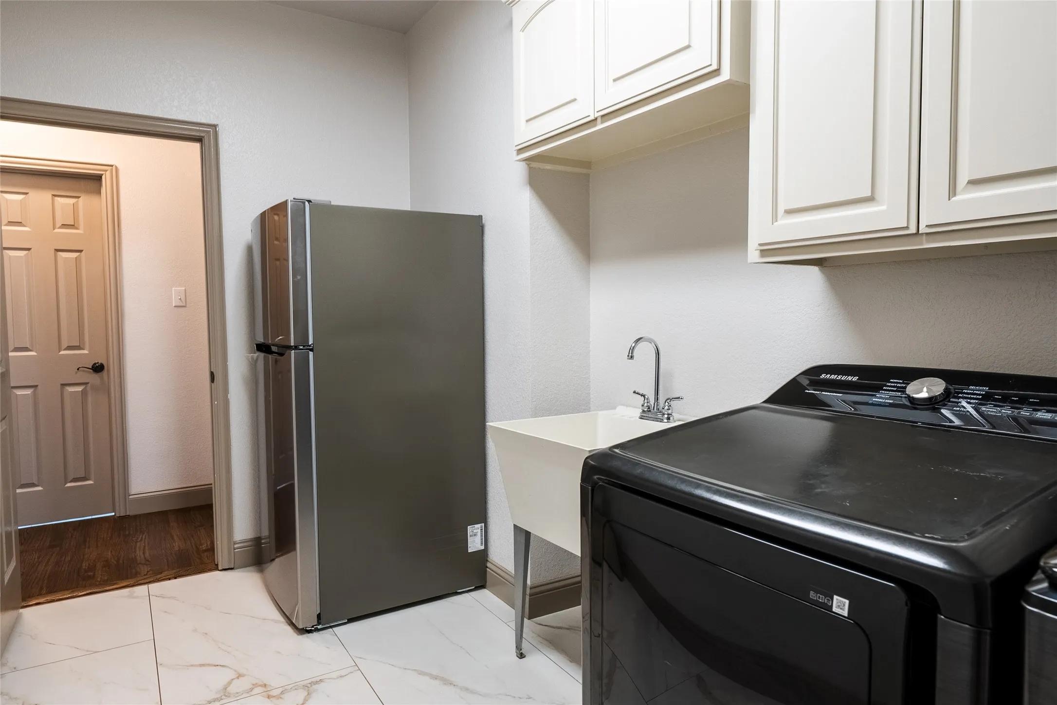 Utility room featuring white shaker-style cabinetry, a built-in utility sink with chrome faucet, and white marble-look tile flooring