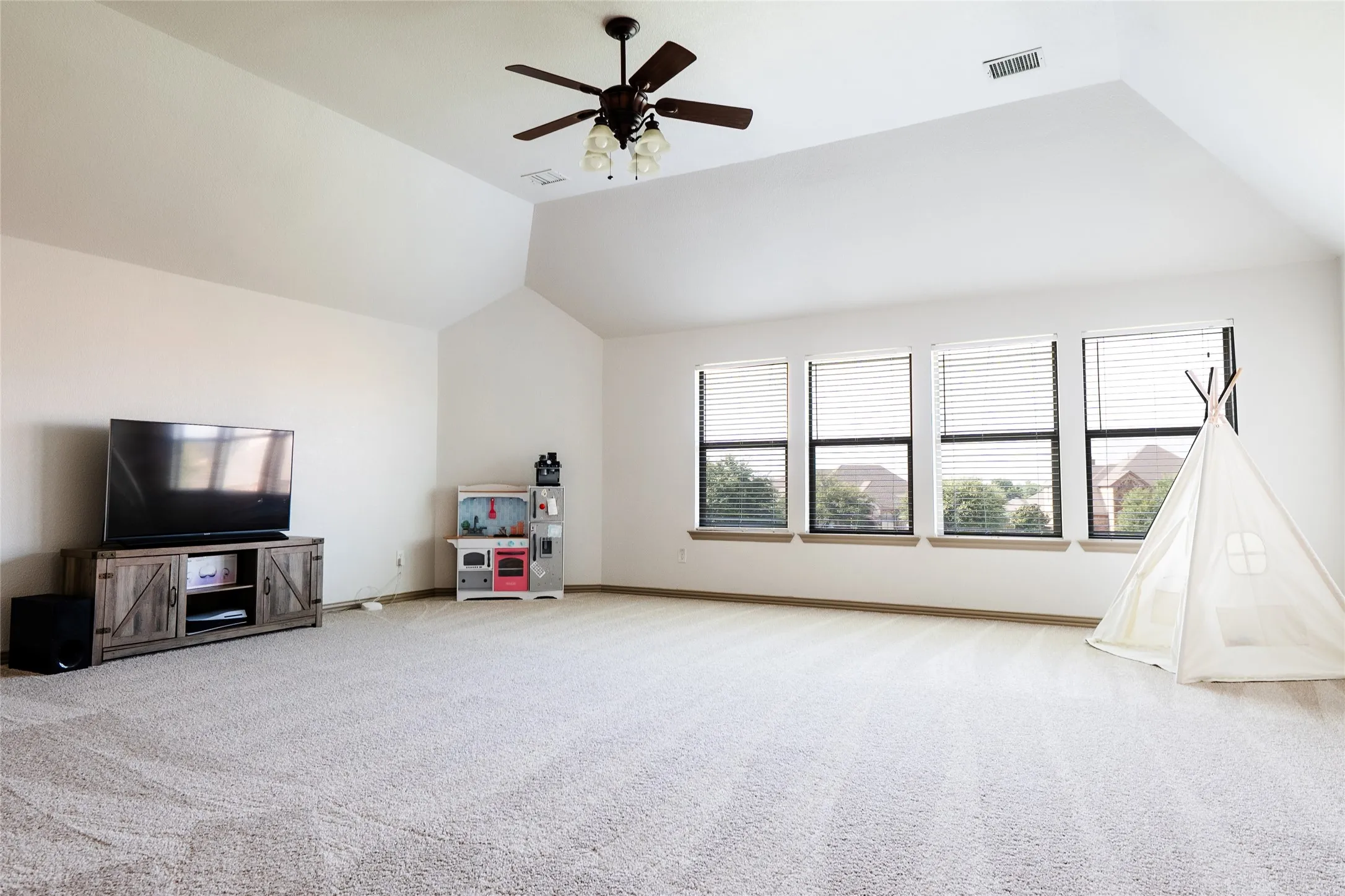 Spacious room featuring vaulted ceilings, light-colored carpeting, and a ceiling fan with integrated lighting