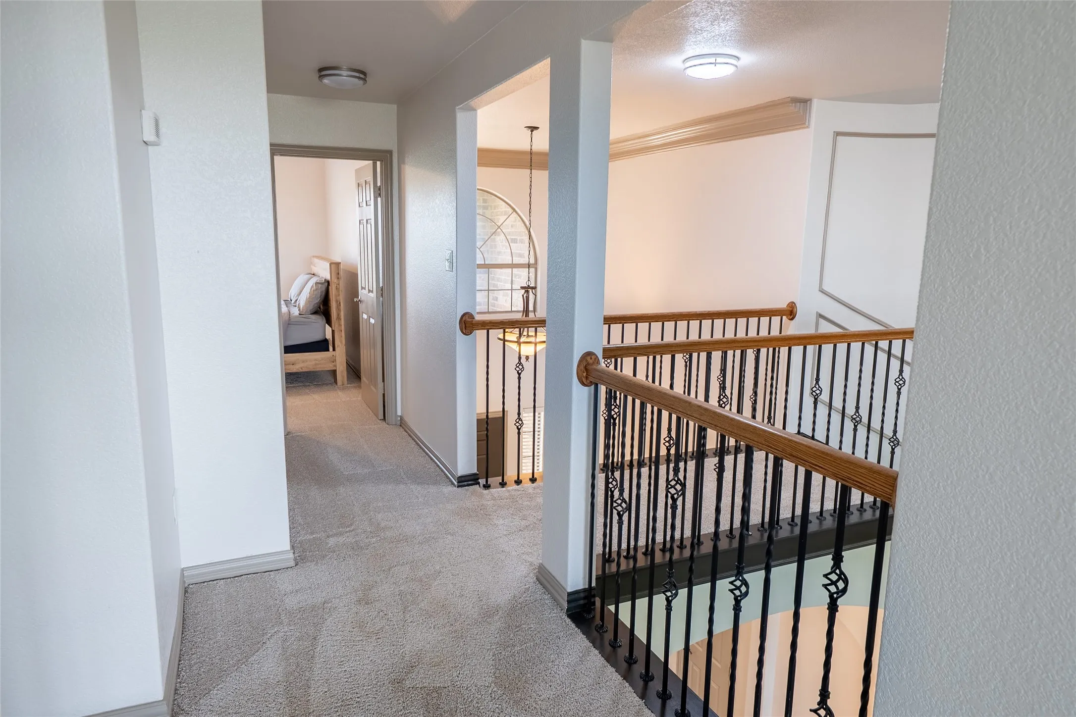 Second-story hallway featuring neutral-toned carpet flooring and a view of the staircase with wrought iron balusters and wood handrails