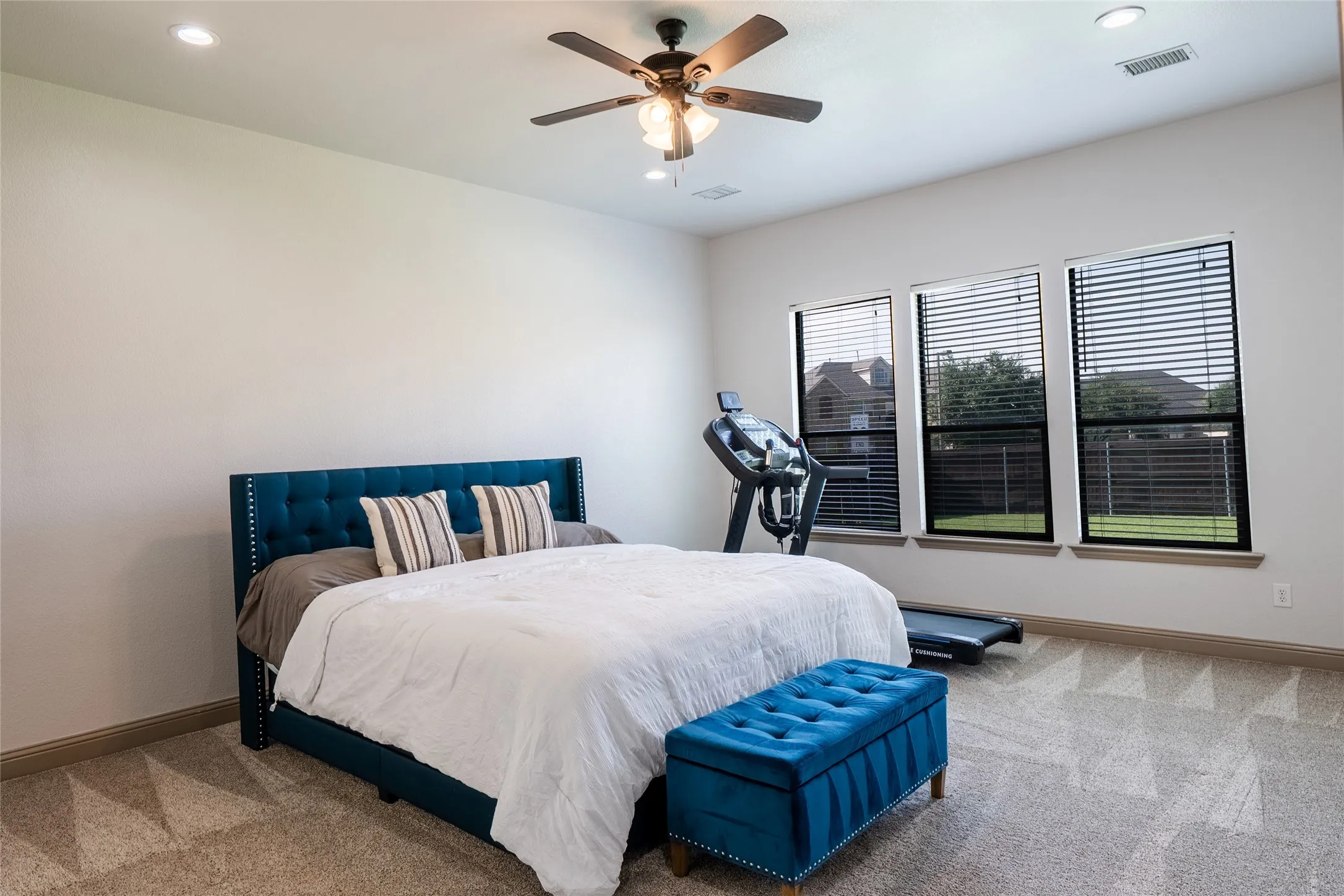 Spacious room featuring three large windows with blinds, recessed lighting, a ceiling fan, and carpeted flooring