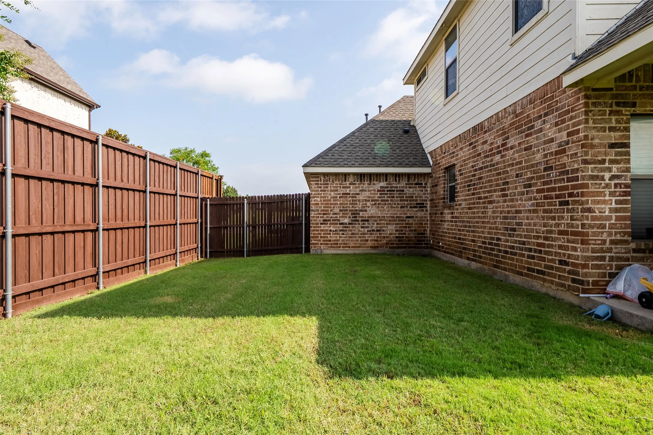 Expansive backyard featuring a manicured lawn, full privacy fencing, and a brick and siding exterior