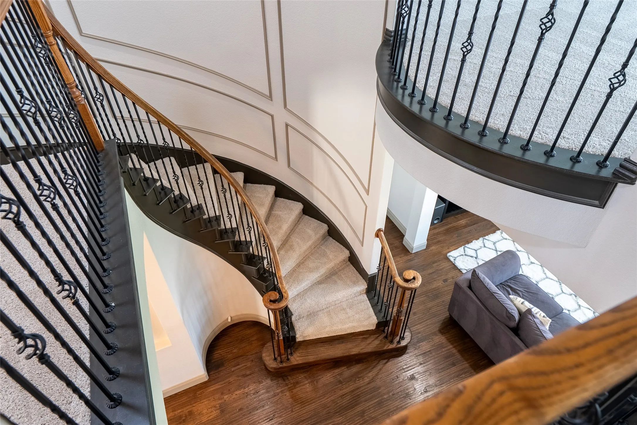 Curved staircase featuring carpeted treads, wrought iron balusters, and a rich wood handrail