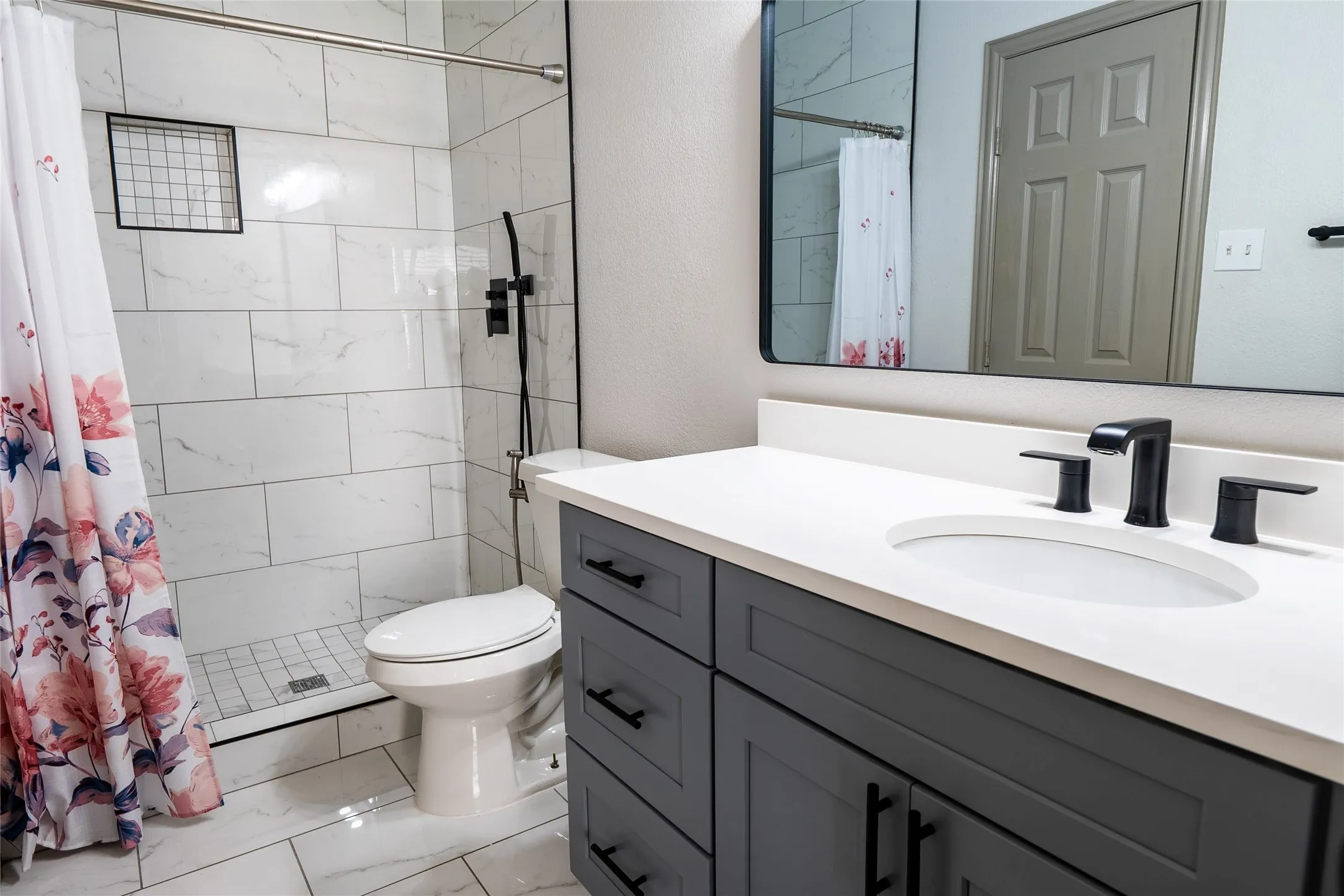 Bathroom featuring a frameless glass shower enclosure, a sleek vanity with a white countertop and oval undermount sink, and dark gray cabinetry with matte black hardware