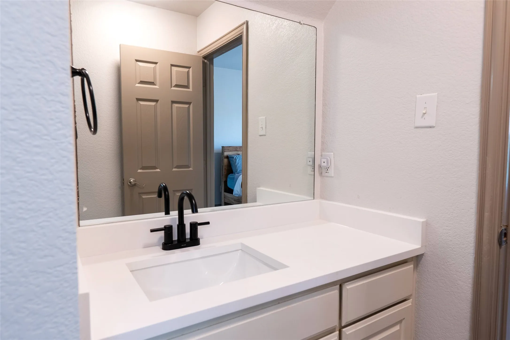 Bathroom vanity featuring an integrated sink, white countertop, matte black faucet, and coordinating towel ring