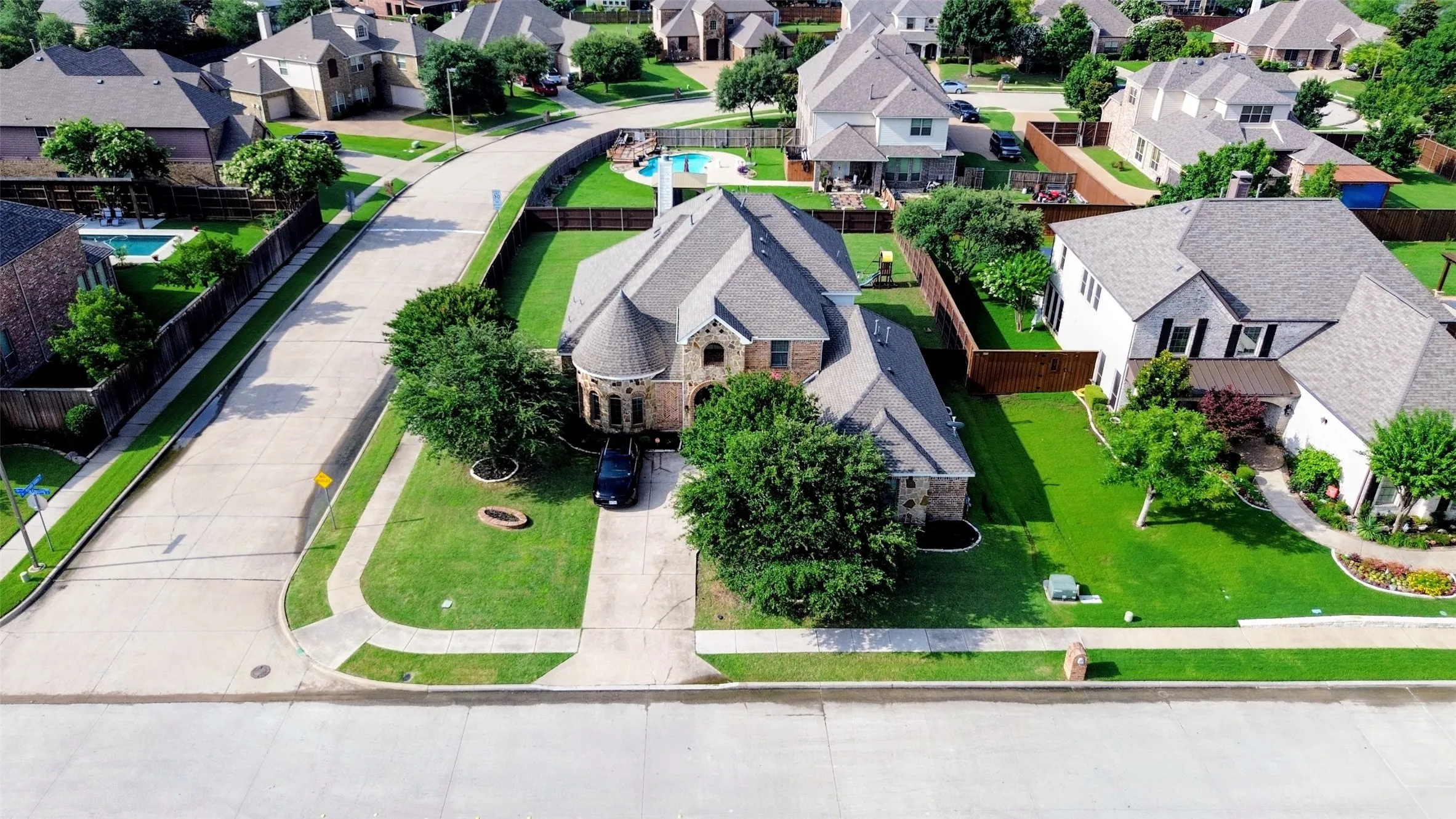 Spacious suburban property featuring a large front yard, mature trees, concrete driveway, and a curved sidewalk