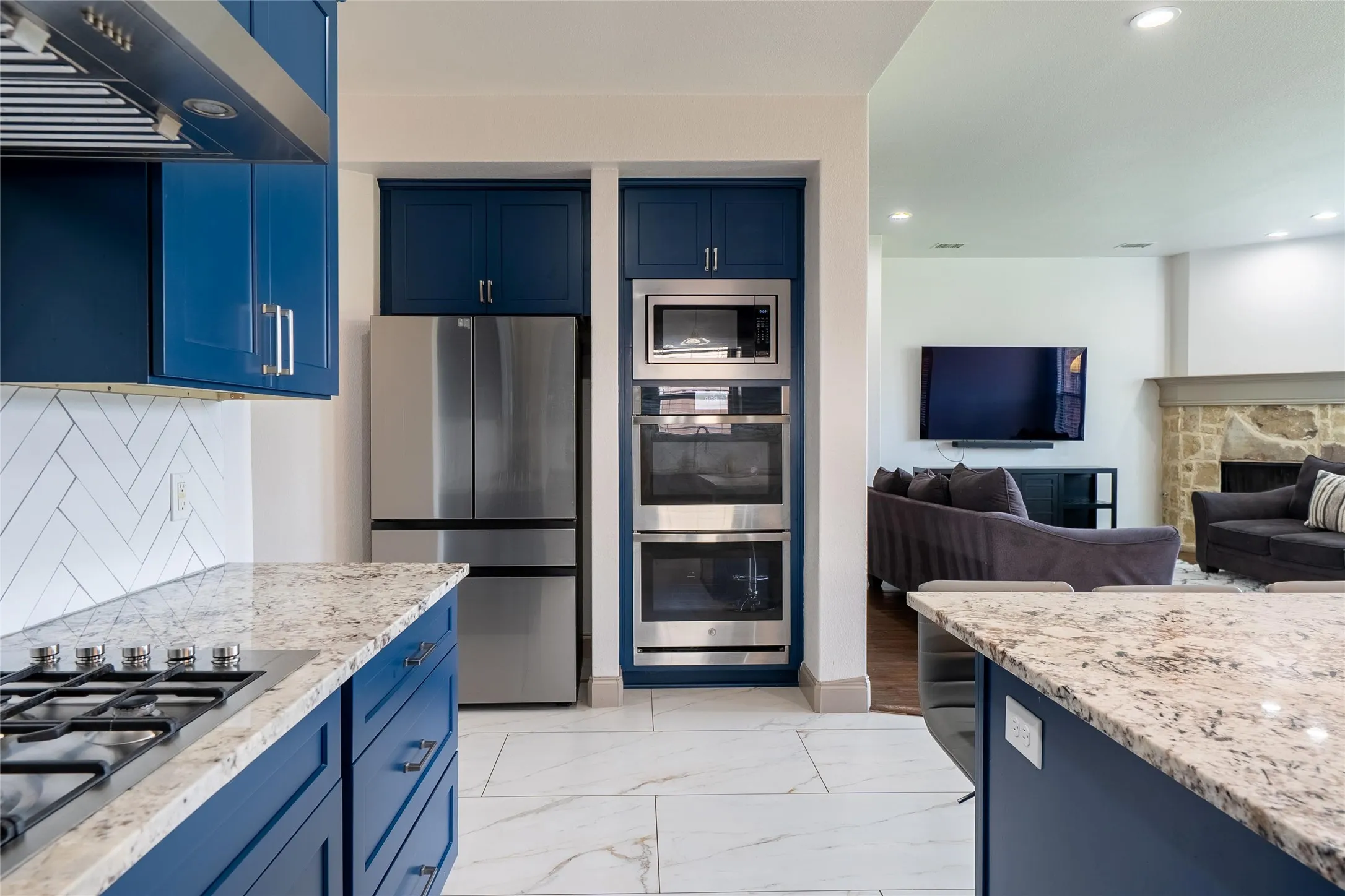 Kitchen featuring blue cabinetry, granite countertops, a gas range, a stainless steel refrigerator, and built-in double ovens