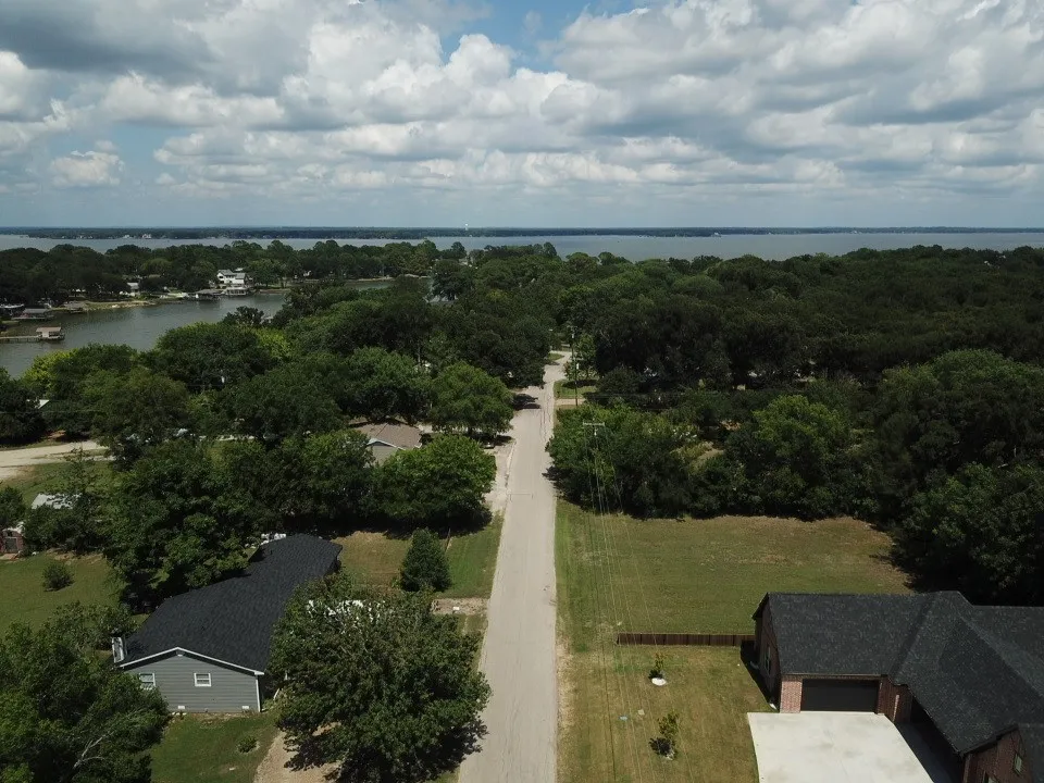 Expansive waterfront community featuring a paved road, mature trees, and a distant body of water.