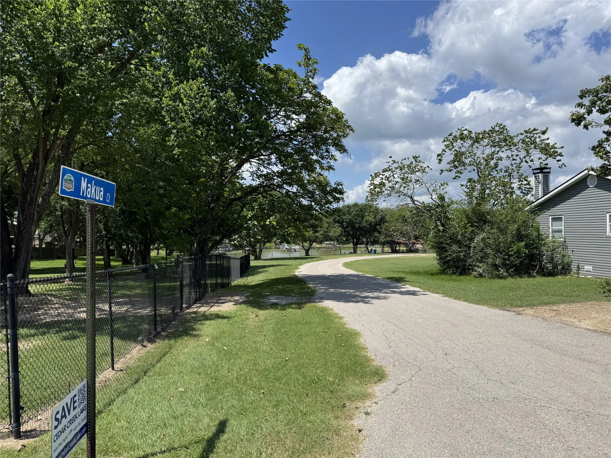 Paved road winding through a residential area with mature trees and green spaces that takes you to the lake a block away.