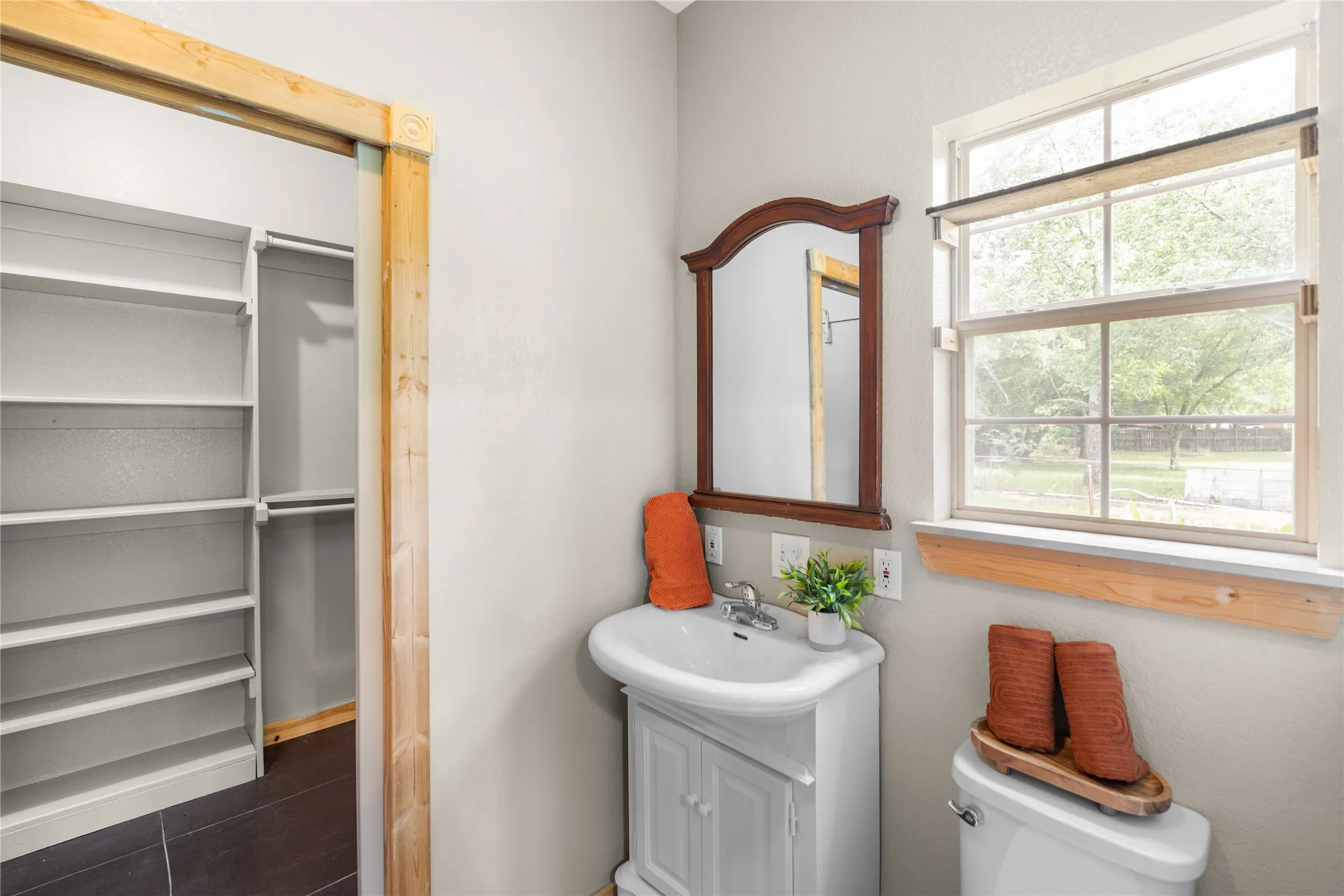 Bathroom featuring a pedestal sink with cabinet storage, a framed mirror, and a window with a wood sill