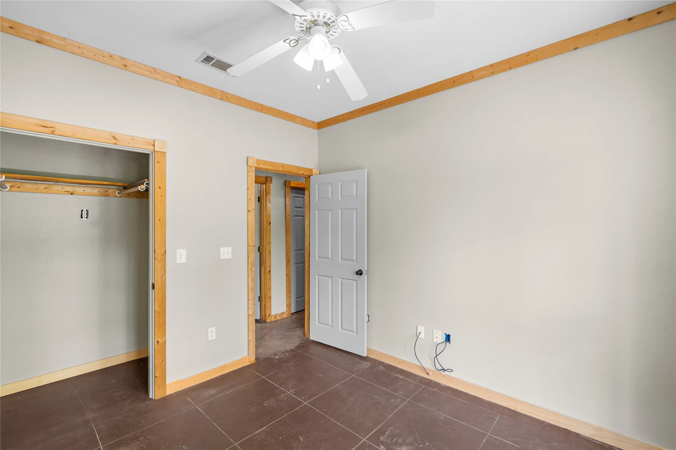 Room featuring brown tile flooring, light gray walls, natural wood-finish trim, and a white ceiling fan with light fixture