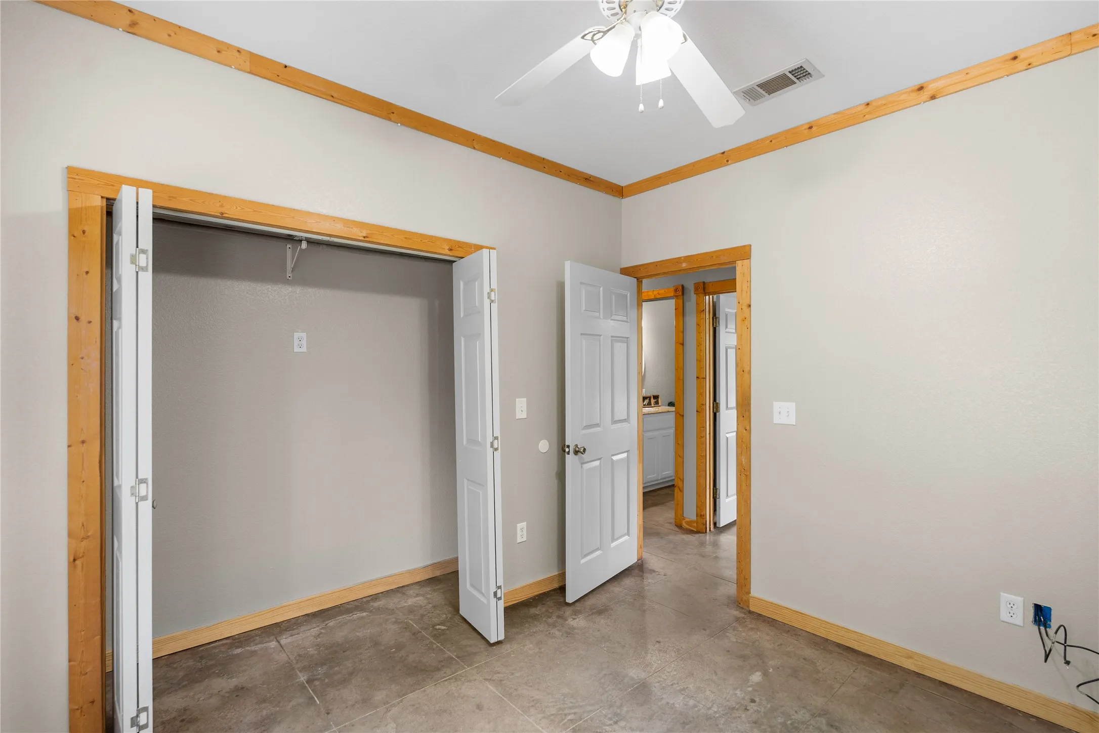 Bedroom featuring concrete flooring, natural wood trim, light gray walls, and a ceiling fan