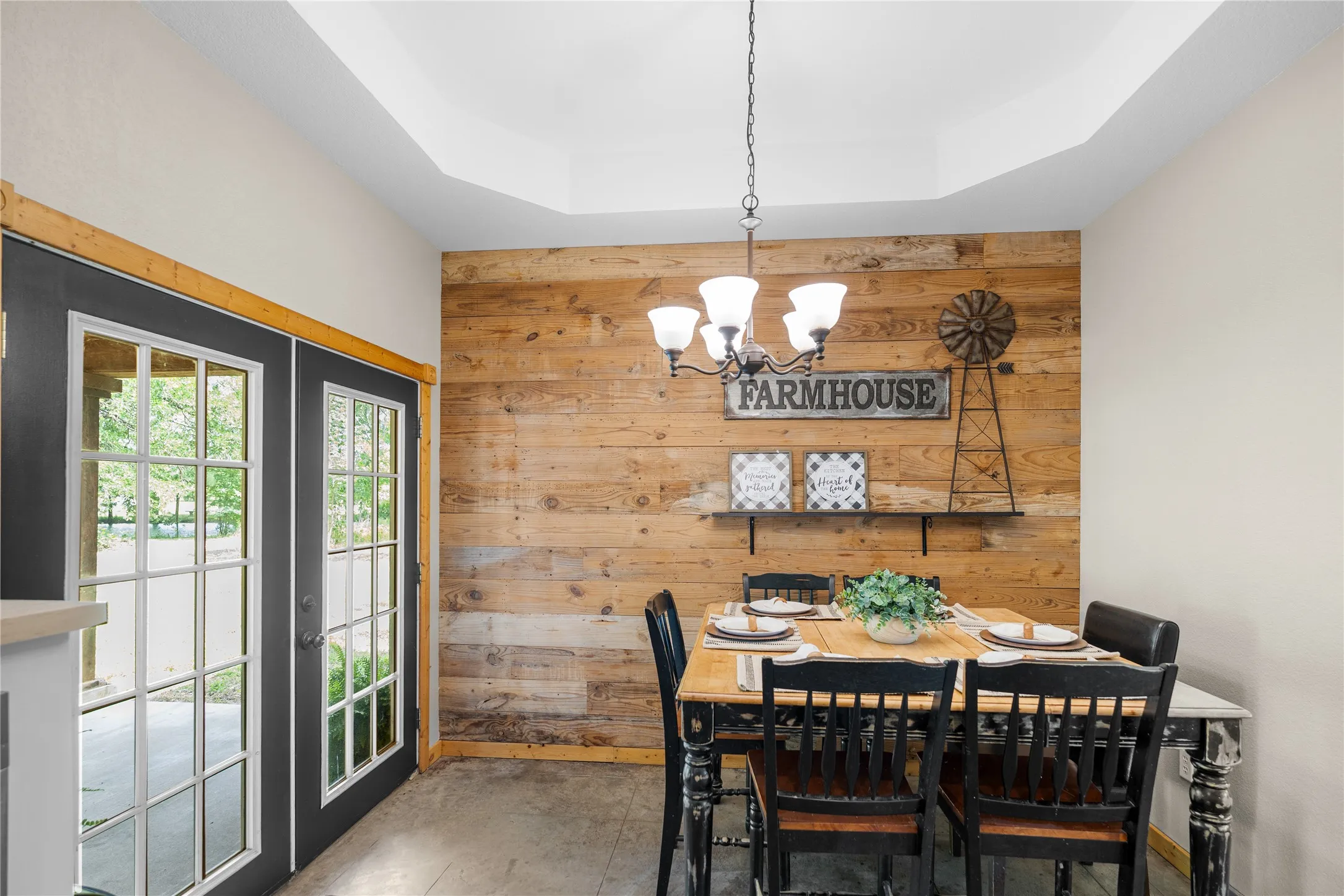 Dining area featuring a wood-panel accent wall, tray ceiling, and a chandelier with decorative shades